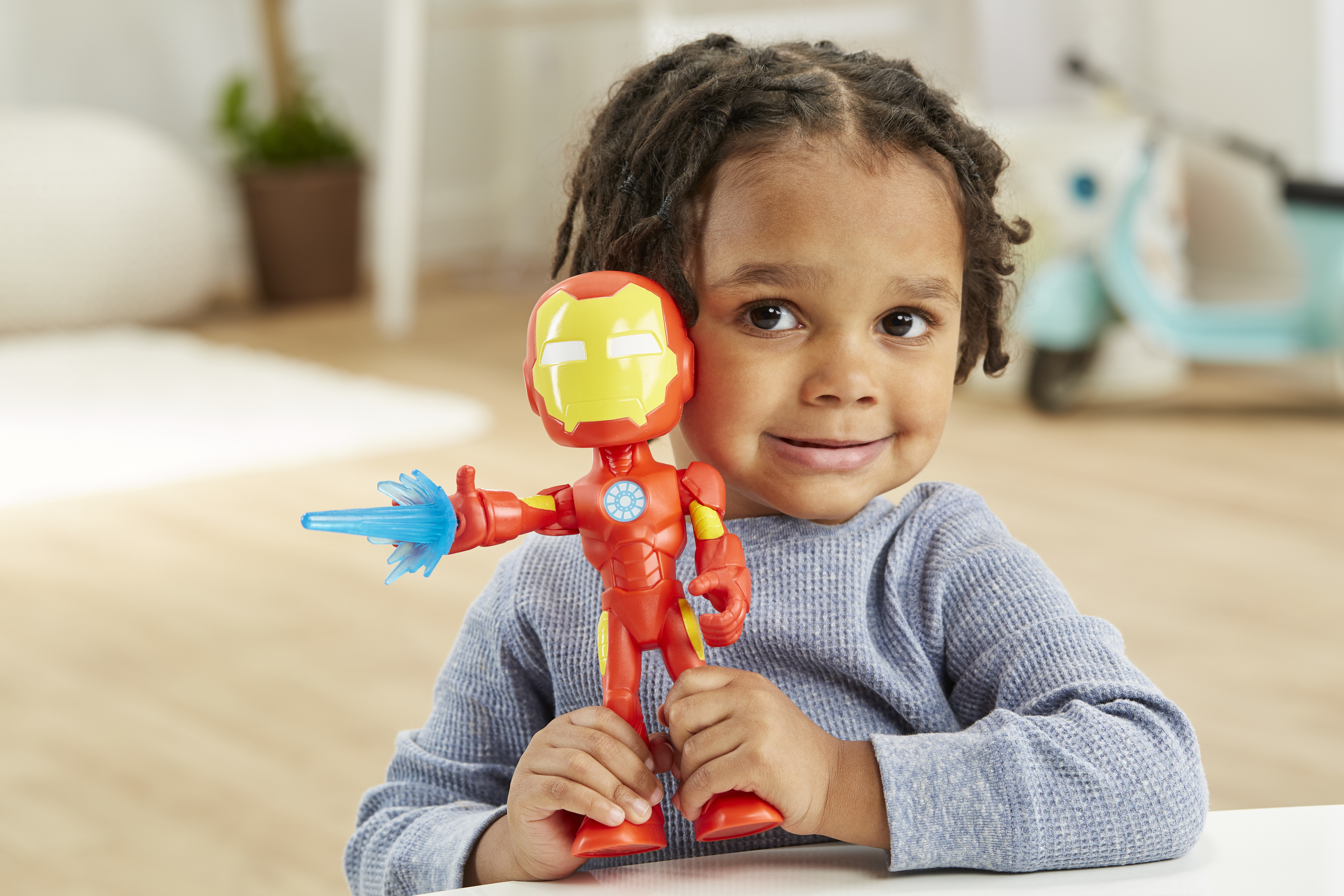 Un bambino tiene in mano un giocattolo di Iron Man. Il giocattolo è rosso e giallo con un'esplosione di energia blu. Il bambino sorride.