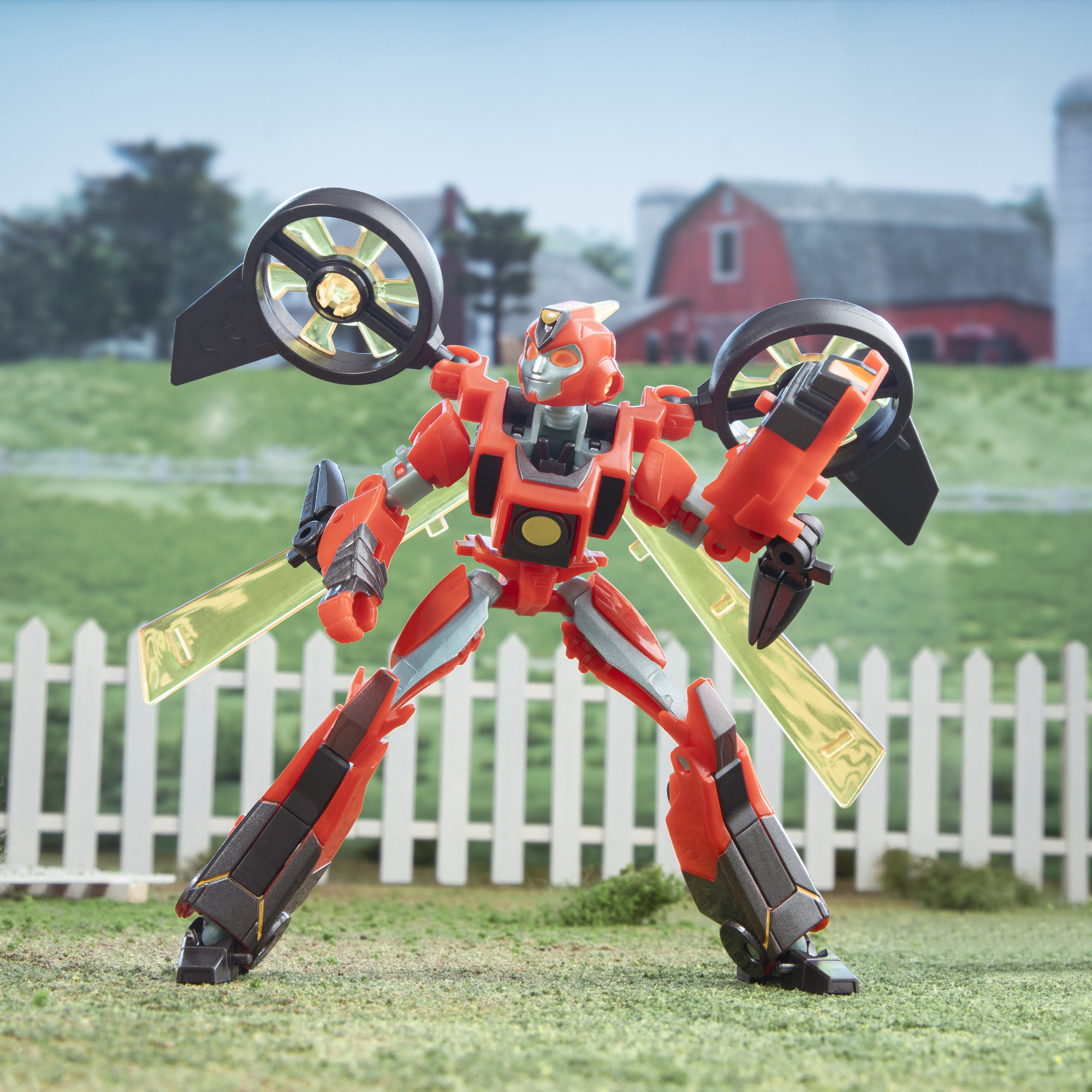 Giocattolo robot rosso sull'erba. Sfondo con recinzione bianca, fattoria e cielo blu.