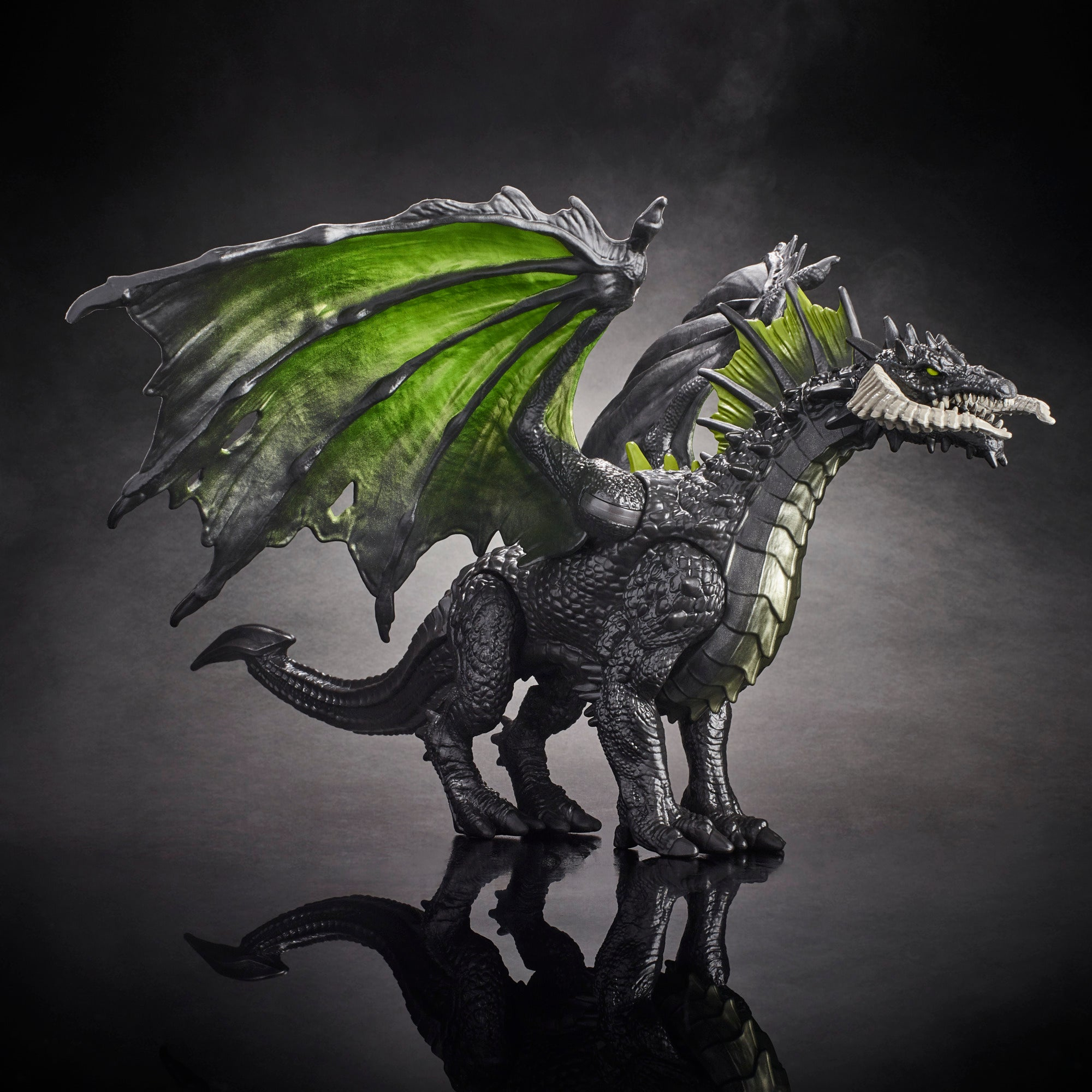 Czarny smok zabawka z zielonymi skrzydłami i żółtymi oczami na odblaskowej powierzchni. Tło jest ciemne.