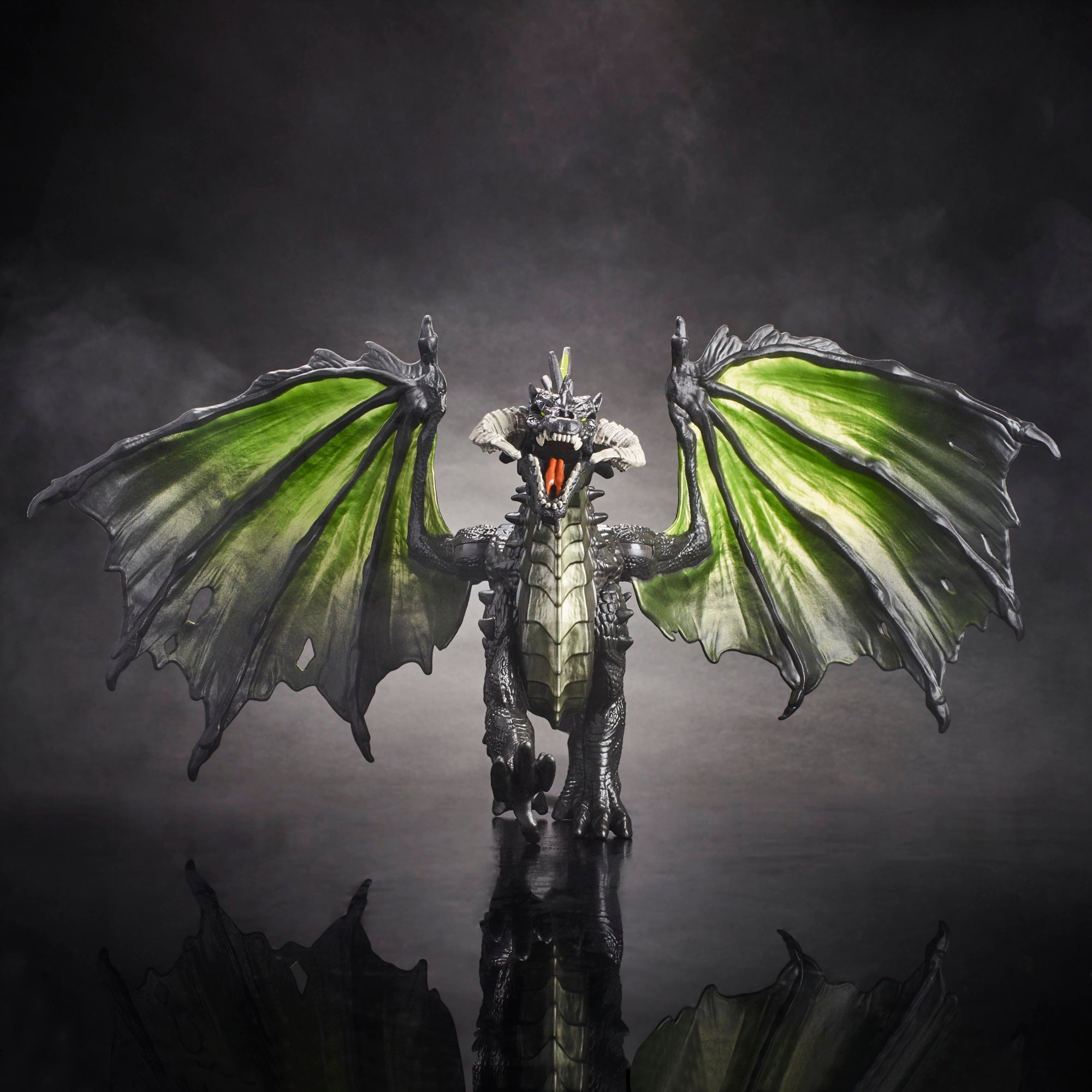 Figurka smoka z zielonymi skrzydłami, otwartą paszczą i ciemną, odbijającą powierzchnią pod spodem.