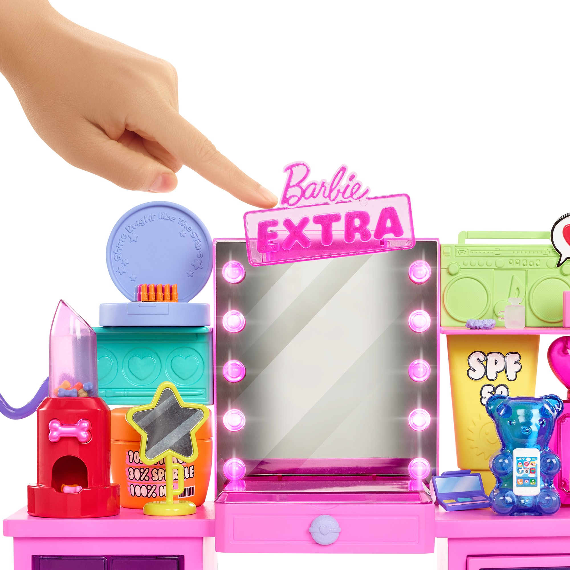 Eine Hand zeigt auf ein Barbie Extra Schminktisch-Set. Es umfasst einen Spiegel, Zubehör und einen bärenförmigen Telefonhalter.