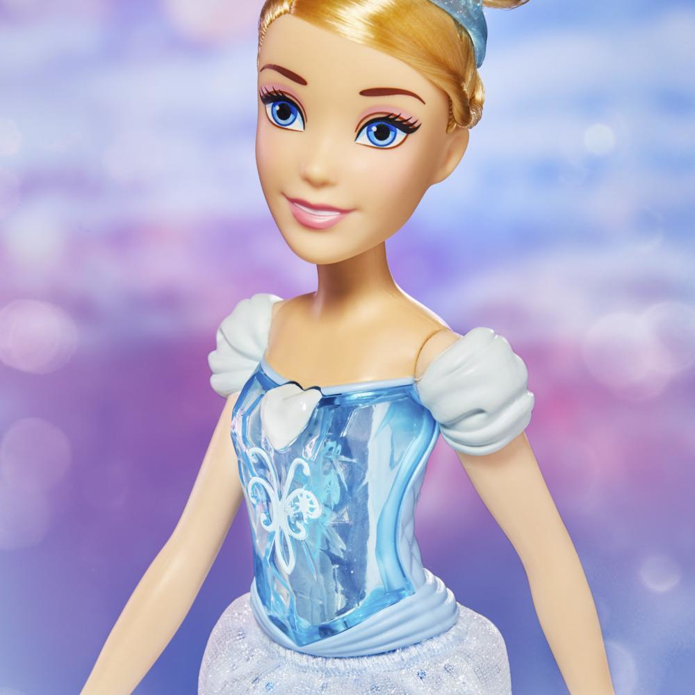 Una muñeca de Cenicienta con cabello rubio, ojos azules y un vestido azul. El fondo es una mezcla borrosa de luces púrpuras y rosas.