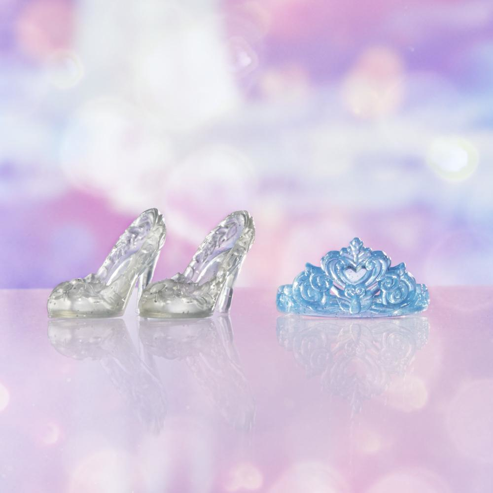La imagen muestra tacones altos transparentes y una tiara azul sobre una superficie reflectante, con un fondo borroso y colorido.