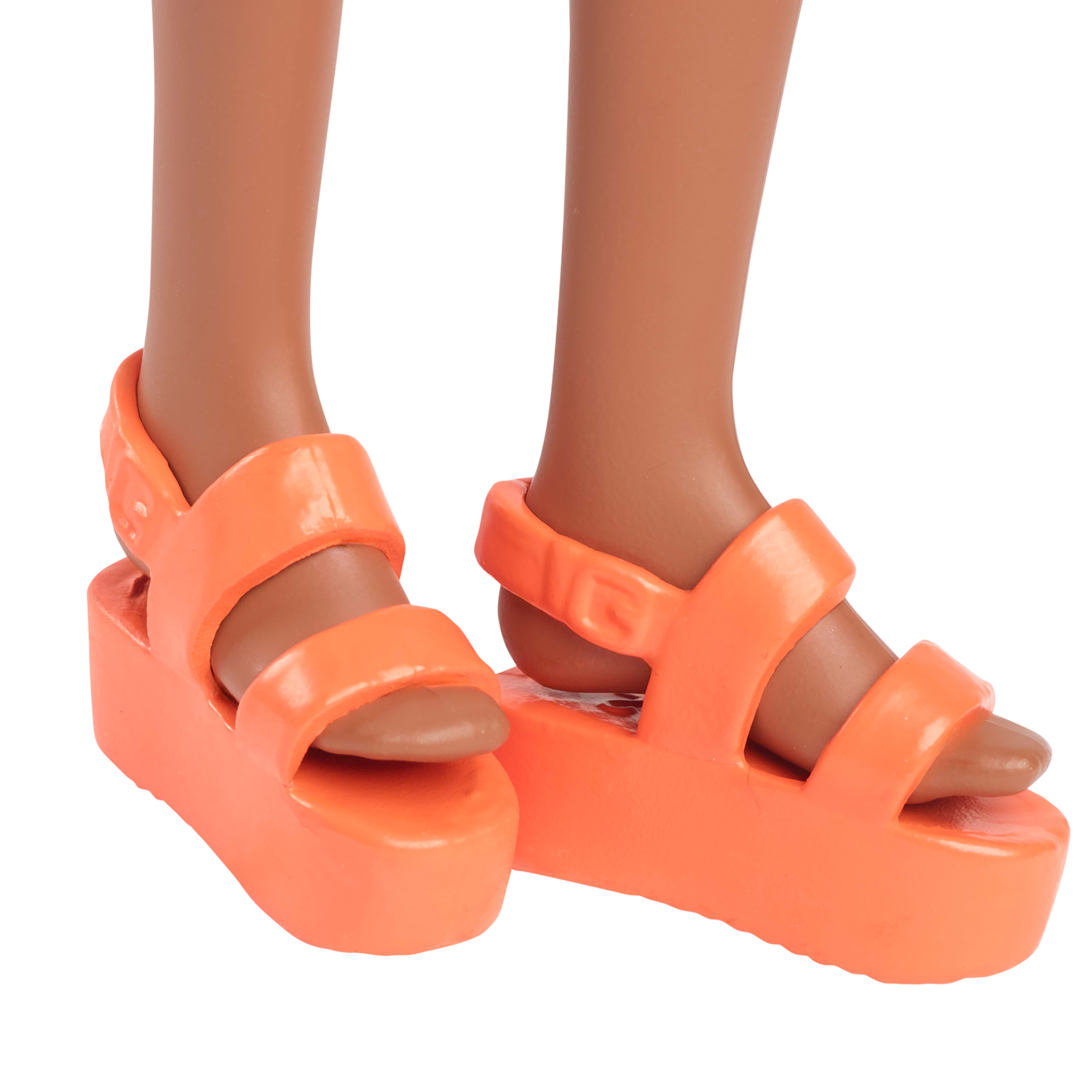 Zbliżenie stóp lalki w jaskrawopomarańczowych sandałach na platformie. Widoczne brązowe stopy.