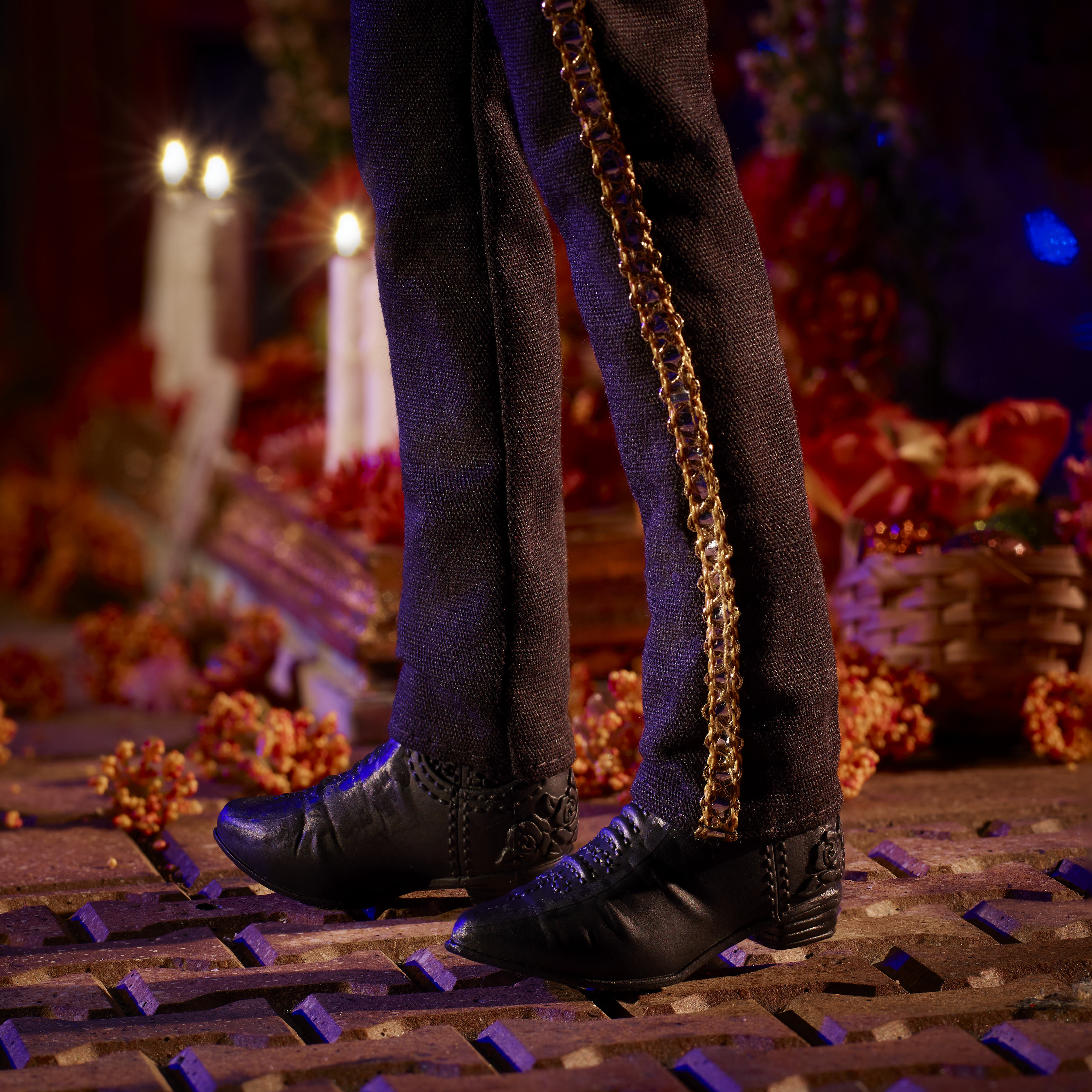 Zbliżenie nóg i butów lalki. Czarne spodnie ze złotymi lamówkami, czarne buty na wzorzystym podłożu.