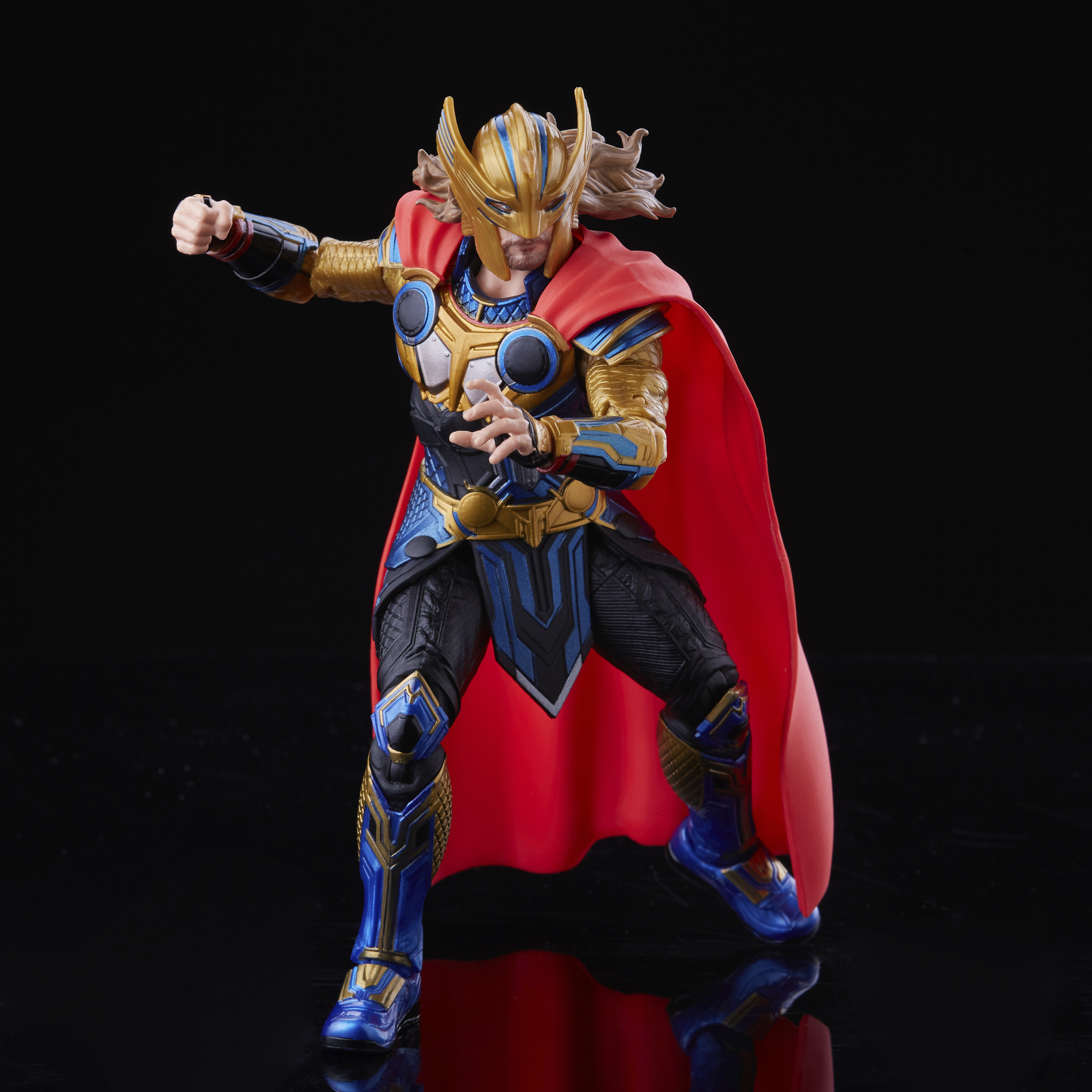 Un action figure di Thor con armatura oro, blu e nera, mantello rosso, su sfondo nero.