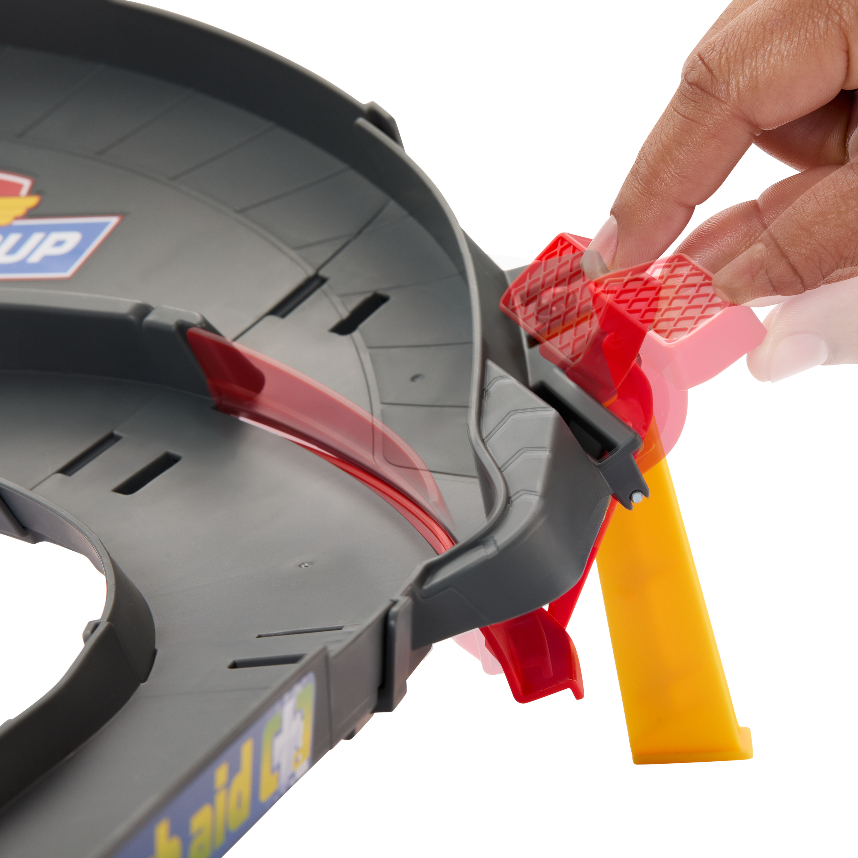 Dłoń wchodzi w interakcję z szarą i czerwoną zabawką toru wyścigowego. Tor ma żółte wsparcie.