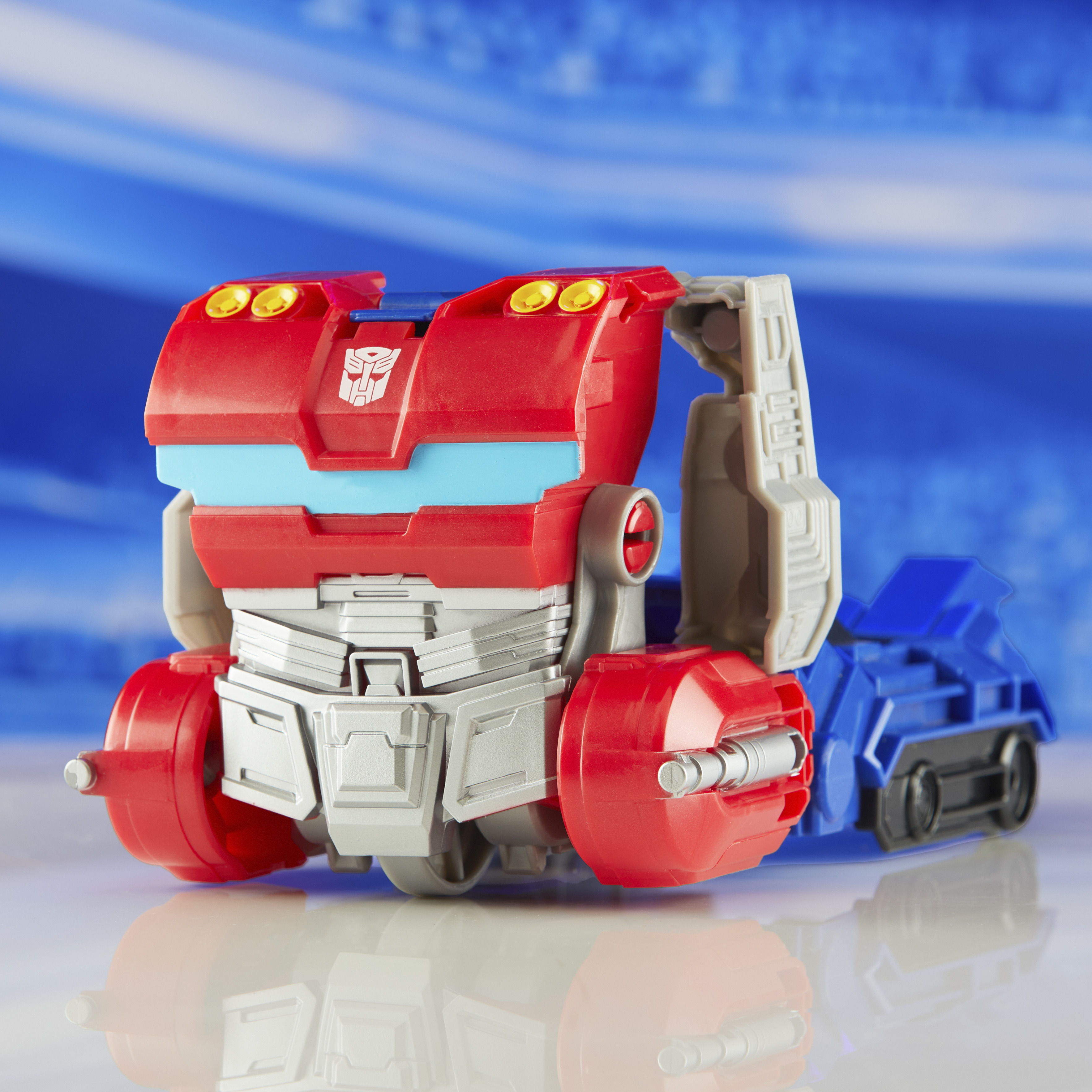Un giocattolo Transformer rosso e blu con sfondo blu. Il giocattolo è su una superficie riflettente.