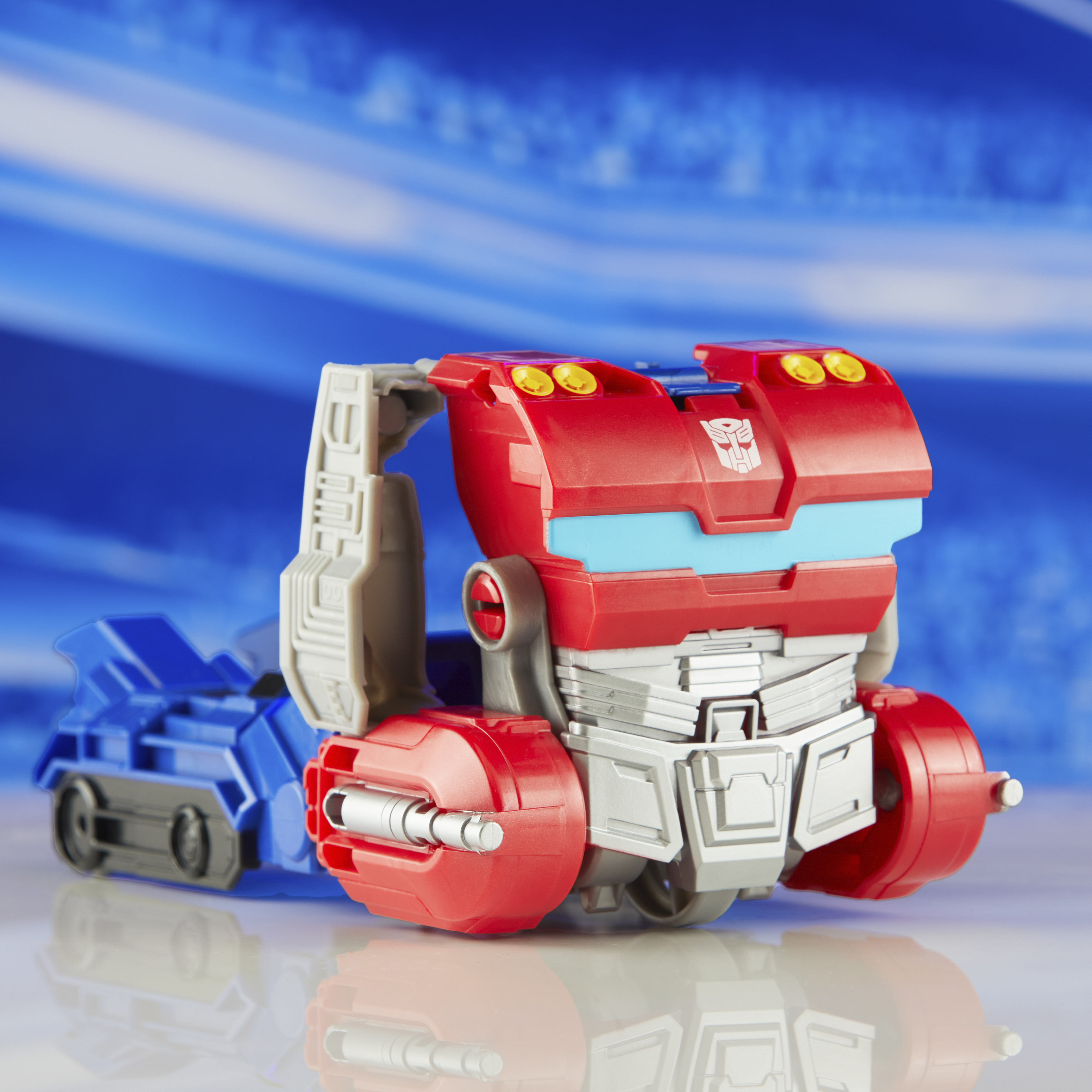 Un giocattolo Transformer rosso e blu è su una superficie riflettente contro uno sfondo blu sfocato.