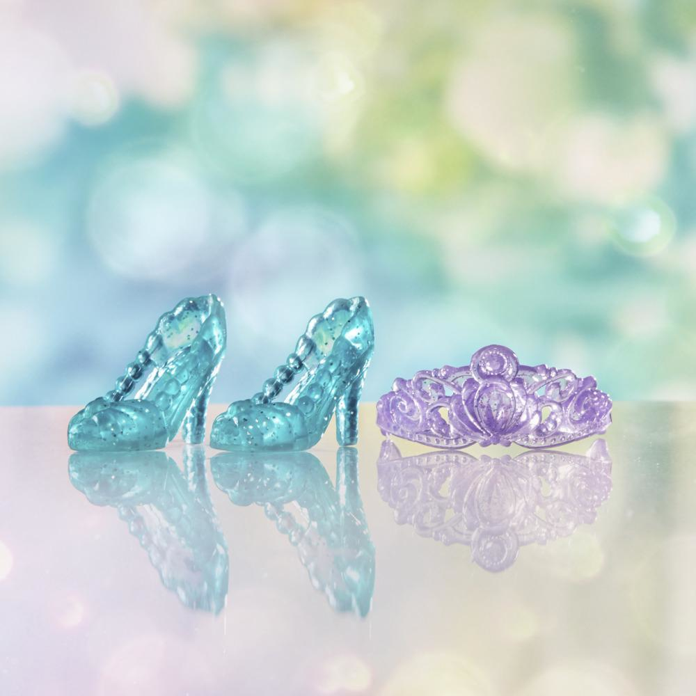 Due scarpette di cristallo blu e una tiara viola su una superficie riflettente, con uno sfondo sfocato e colorato.