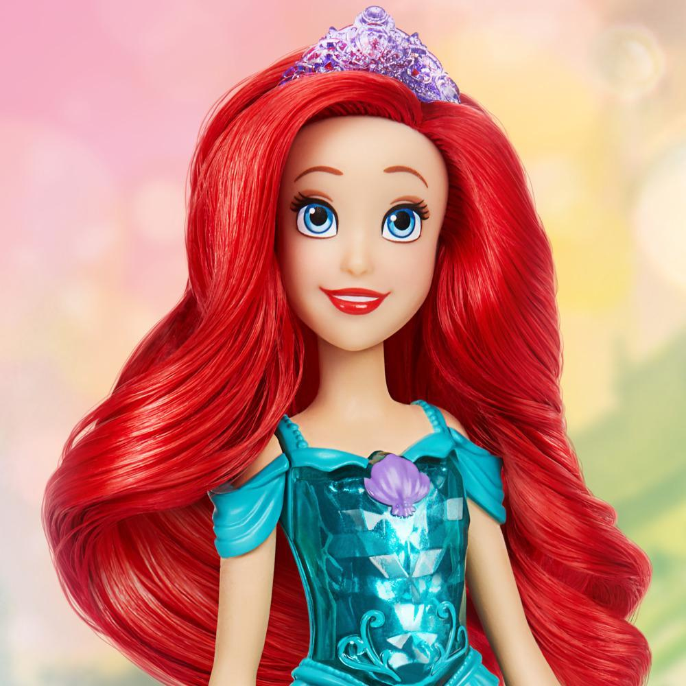Bambola di Ariel con capelli rossi, occhi blu e tiara. Indossa un vestito turchese con una conchiglia. Sfondo sfocato rosa e giallo.