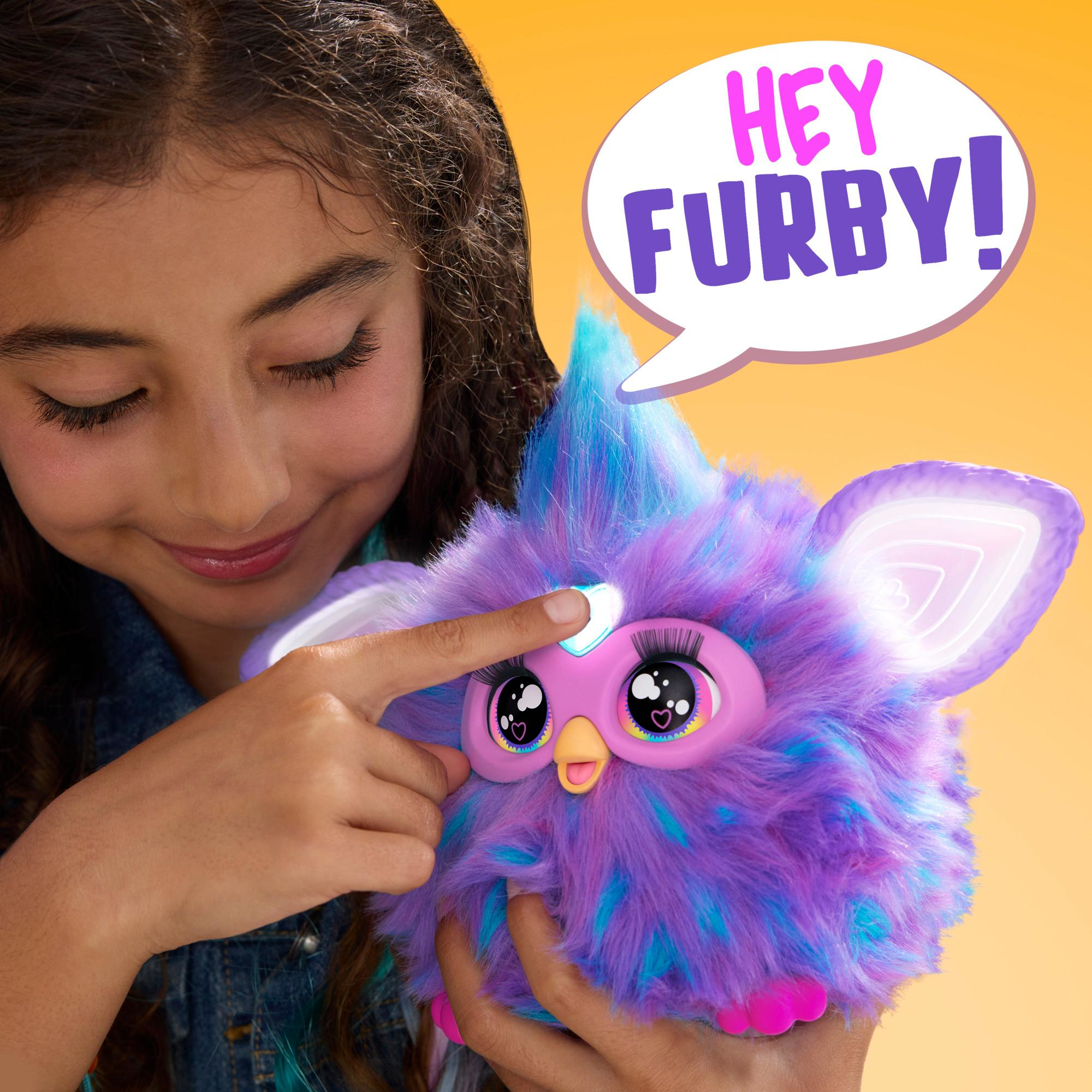 Ein Mädchen berührt ein lila Furby-Spielzeug mit blauen Akzenten. Eine Sprechblase sagt 'Hey Furby!'. Der Hintergrund ist gelb.