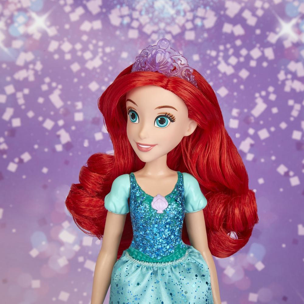 Bambola di Ariel con capelli rossi, occhi blu e tiara viola. Indossa un vestito blu con un fiore. Lo sfondo è viola con glitter.