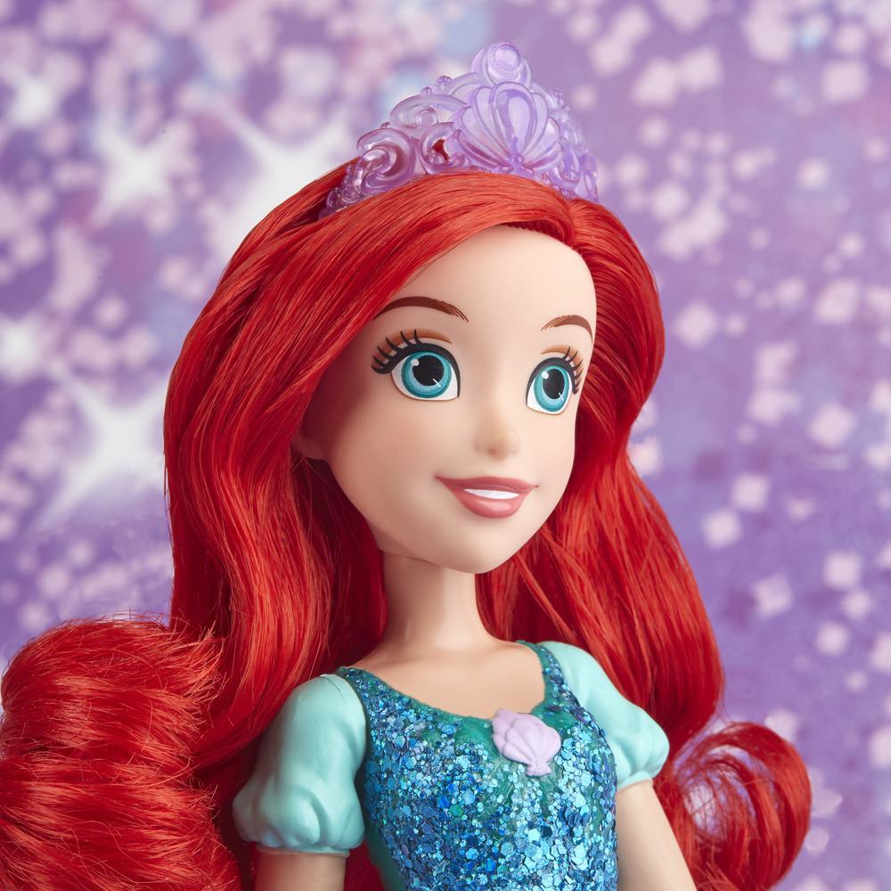 Bambola di Ariel con capelli rossi, occhi blu e tiara viola. Indossa un vestito blu con una conchiglia. Sfondo viola scintillante.