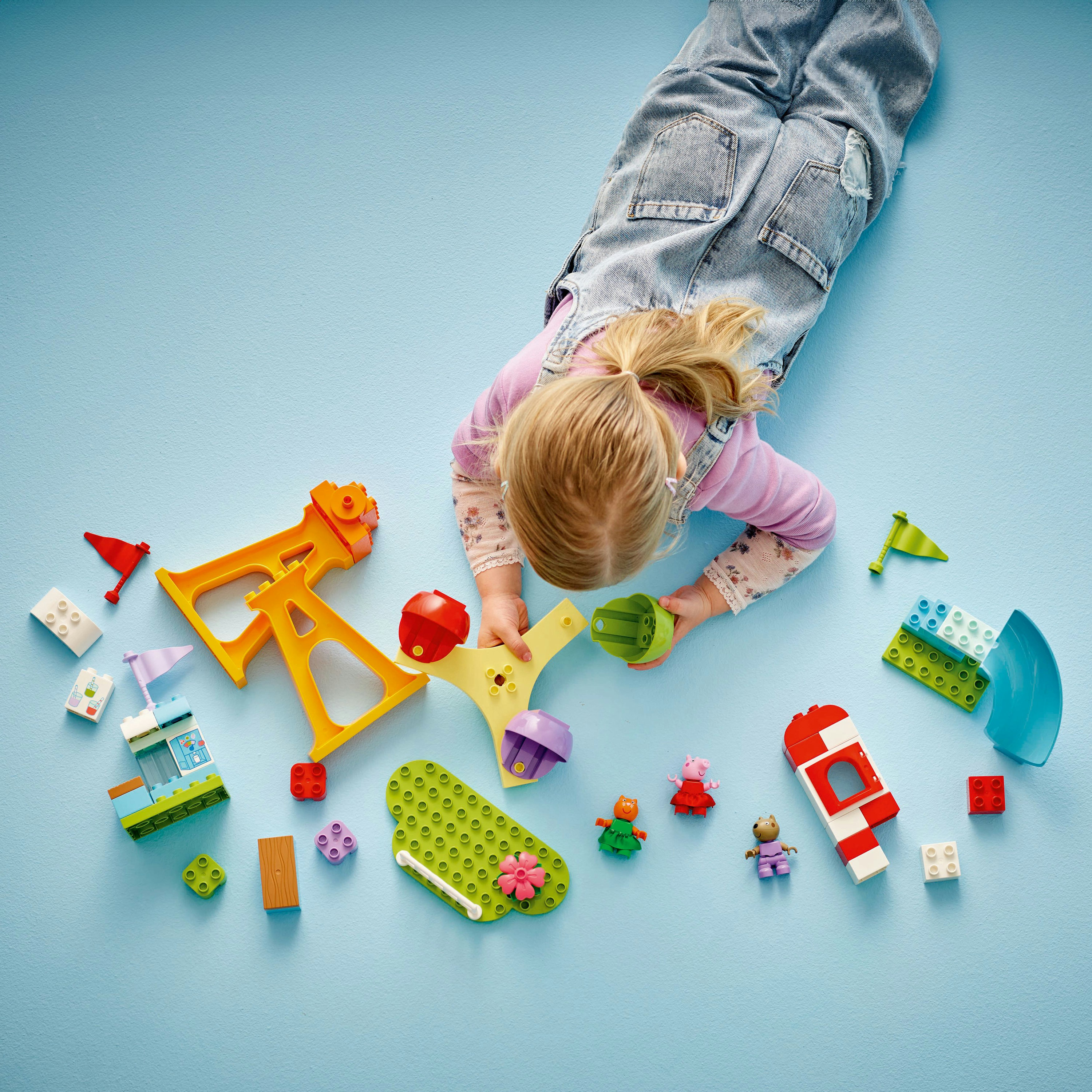 Dziecko bawi się kolorowymi klockami i figurkami na niebieskiej powierzchni. Dziecko leży.