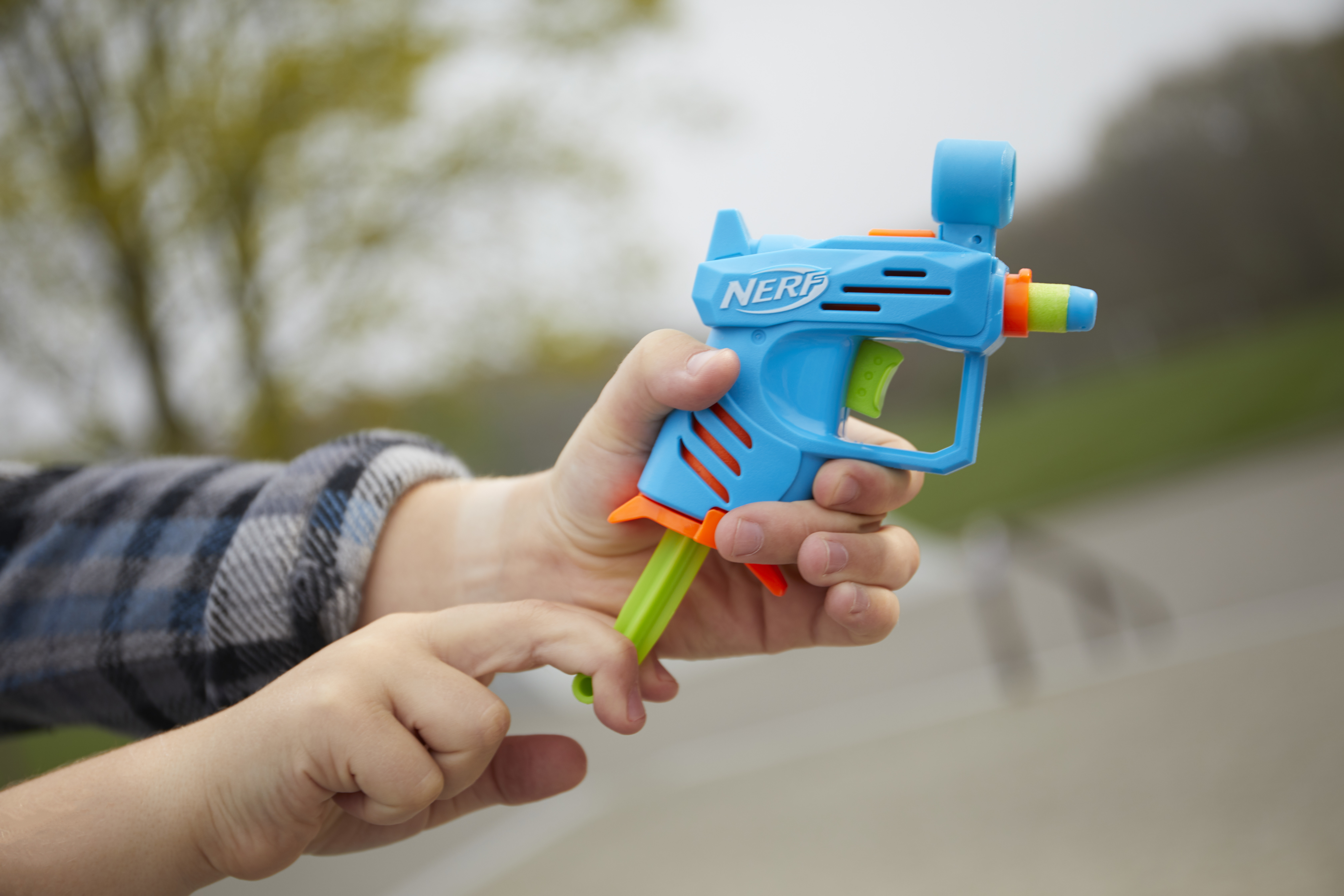 Osoba trzyma niebieski pistolet na wodę Nerf. Pistolet ma pomarańczowe i zielone akcenty. Tło jest rozmyte.