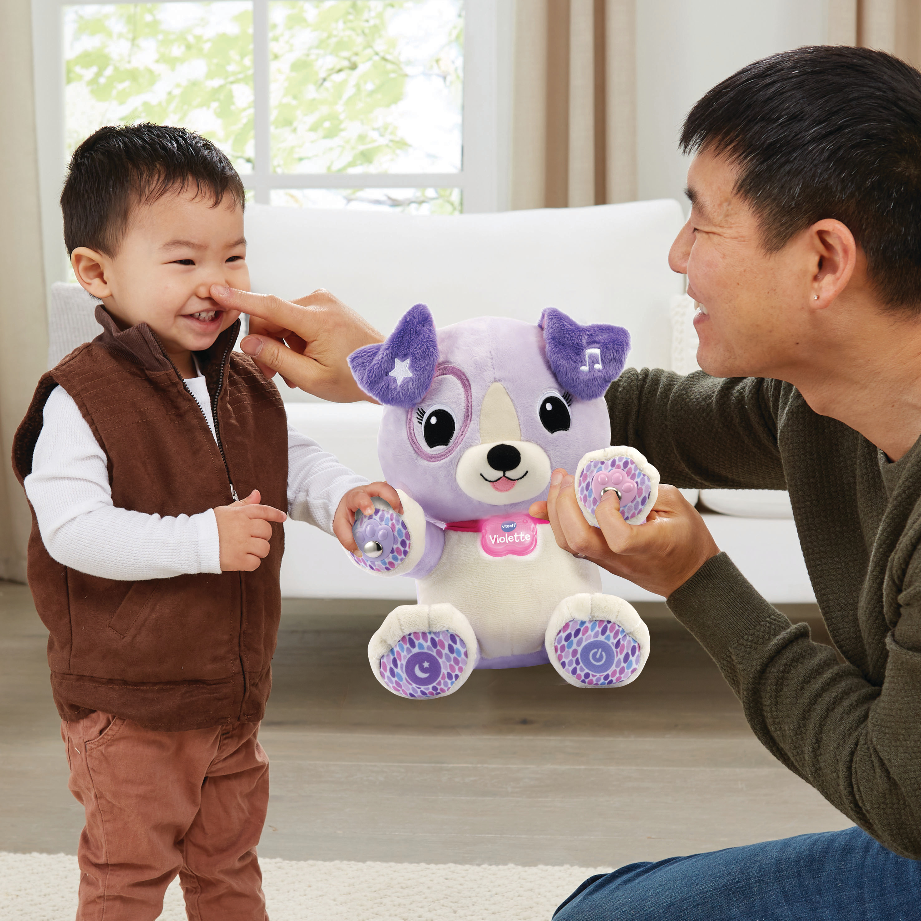 Un homme et un enfant jouent avec un jouet en forme de chien violet. L'enfant rit pendant que l'homme lui touche le nez.