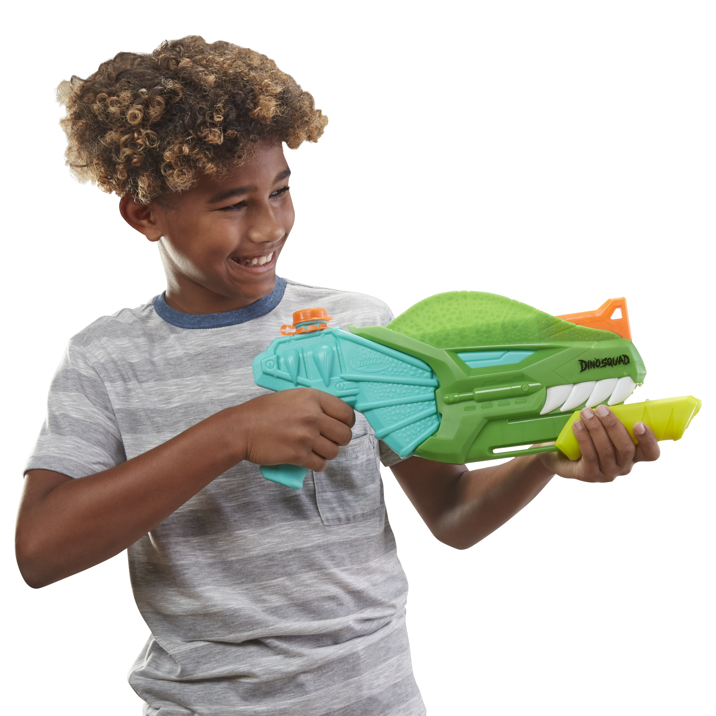 Un ragazzo sorridente tiene in mano una pistola ad acqua a forma di dinosauro verde e blu. Indossa una maglietta grigia a righe e ha i capelli ricci.