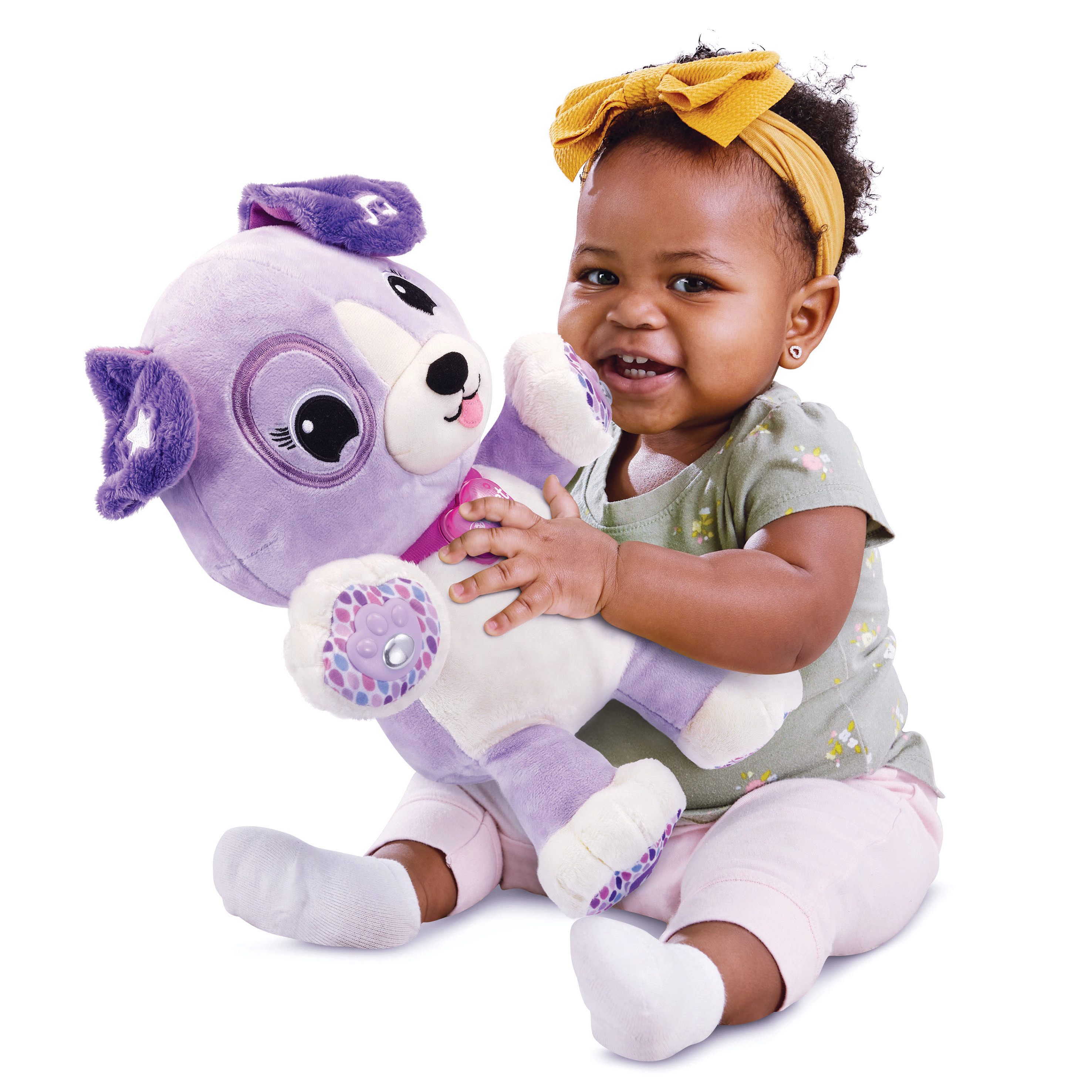 Un bébé souriant tient un jouet en peluche de chiot violet. Elle porte un bandeau jaune et un pantalon rose.