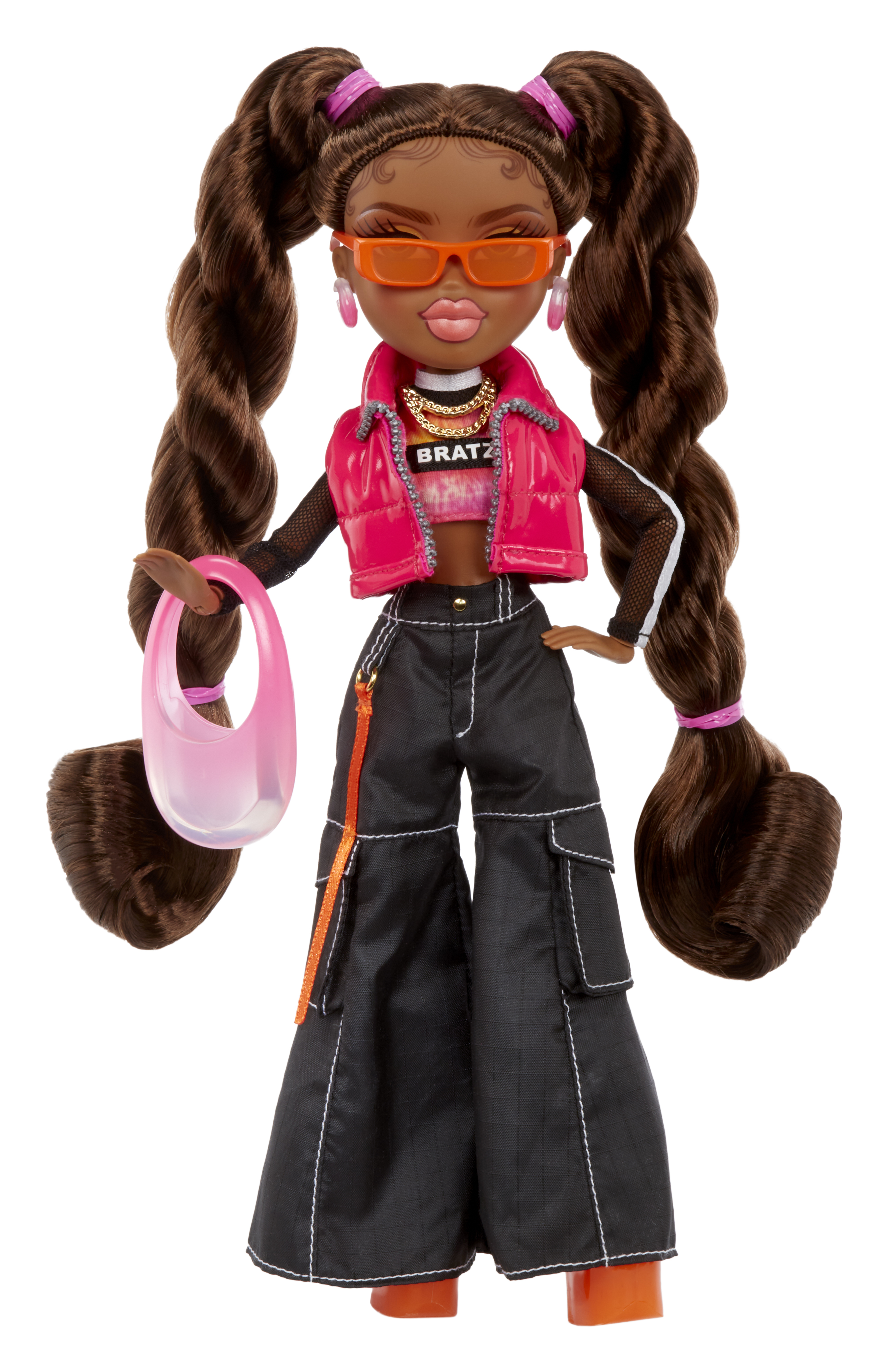 Lalka z długimi brązowymi warkoczami, pomarańczowymi okularami, różową kurtką, czarnymi spodniami trzymająca różową torebkę.