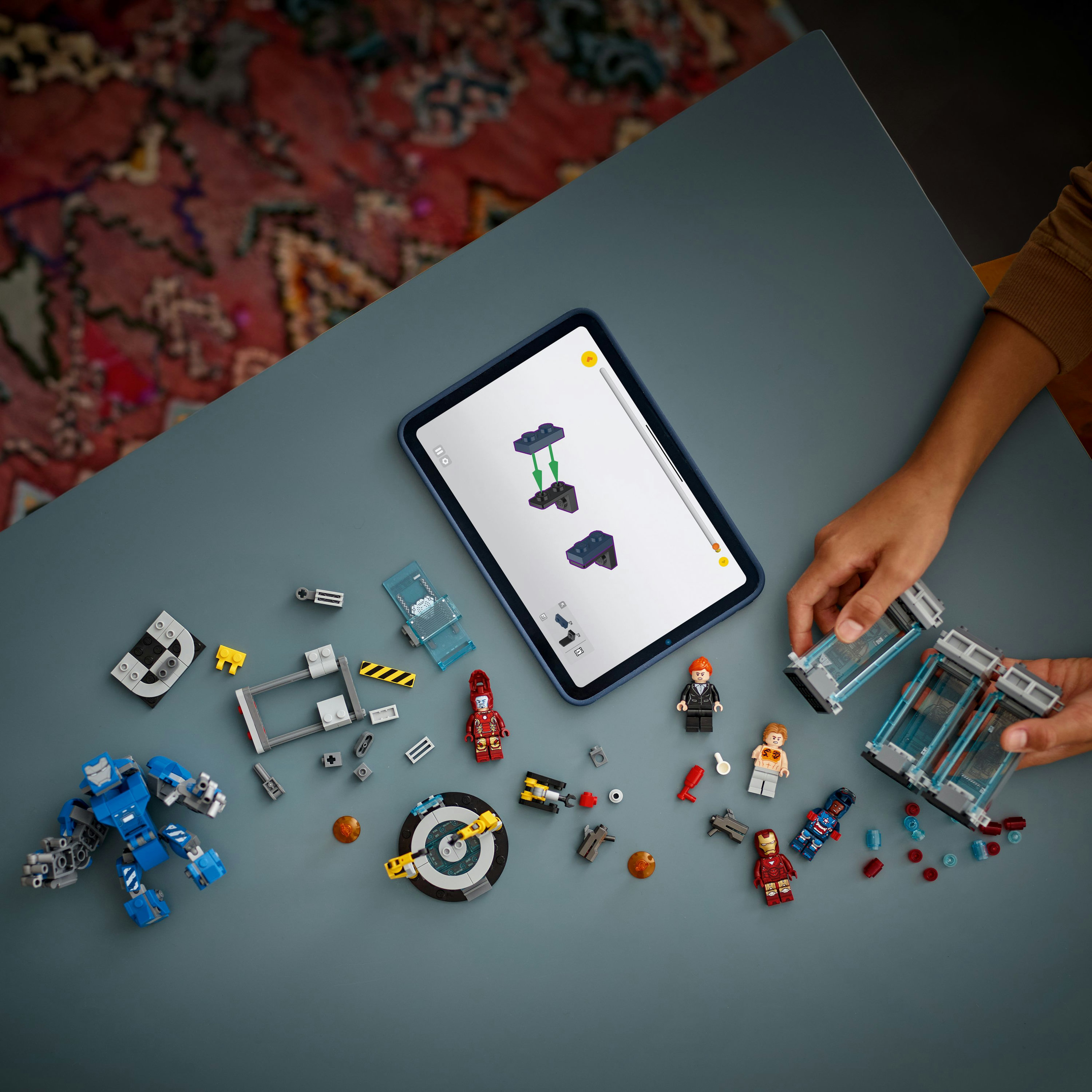 Stół z klockami Lego, tablet z instrukcjami i dłonie trzymające klocki Lego. Widoczne kilka figurek Lego.
