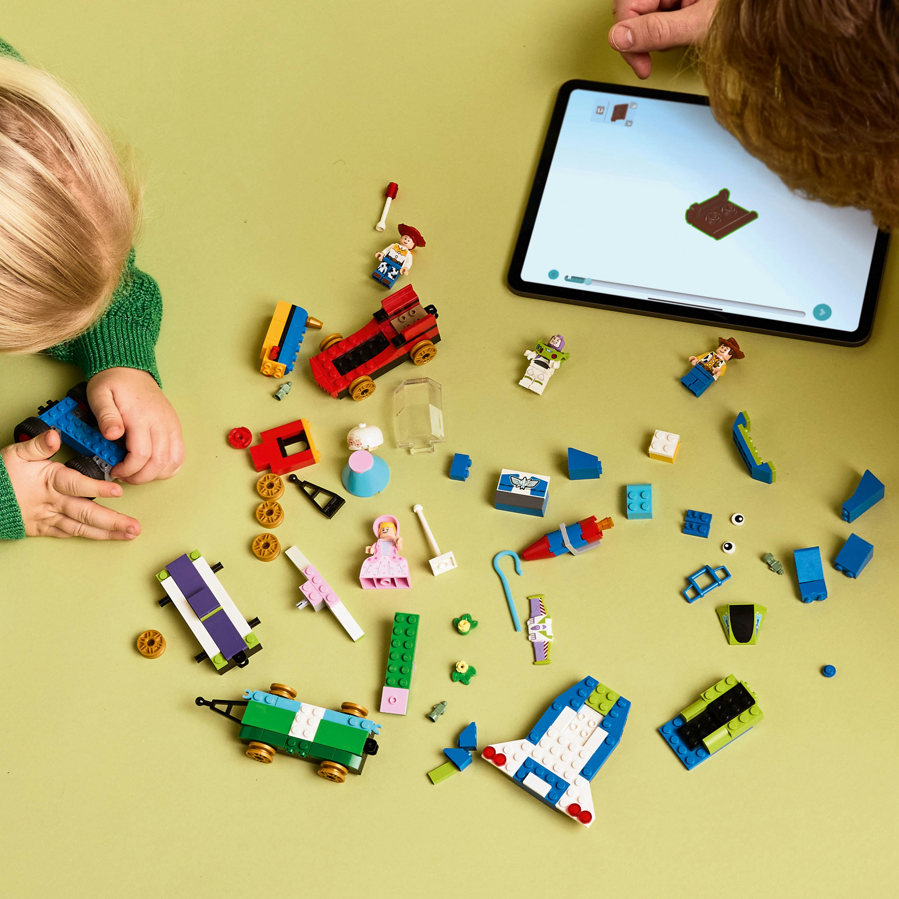 Dzieci bawią się klockami Lego. Kilka postaci Lego i tablet na zielonej powierzchni.