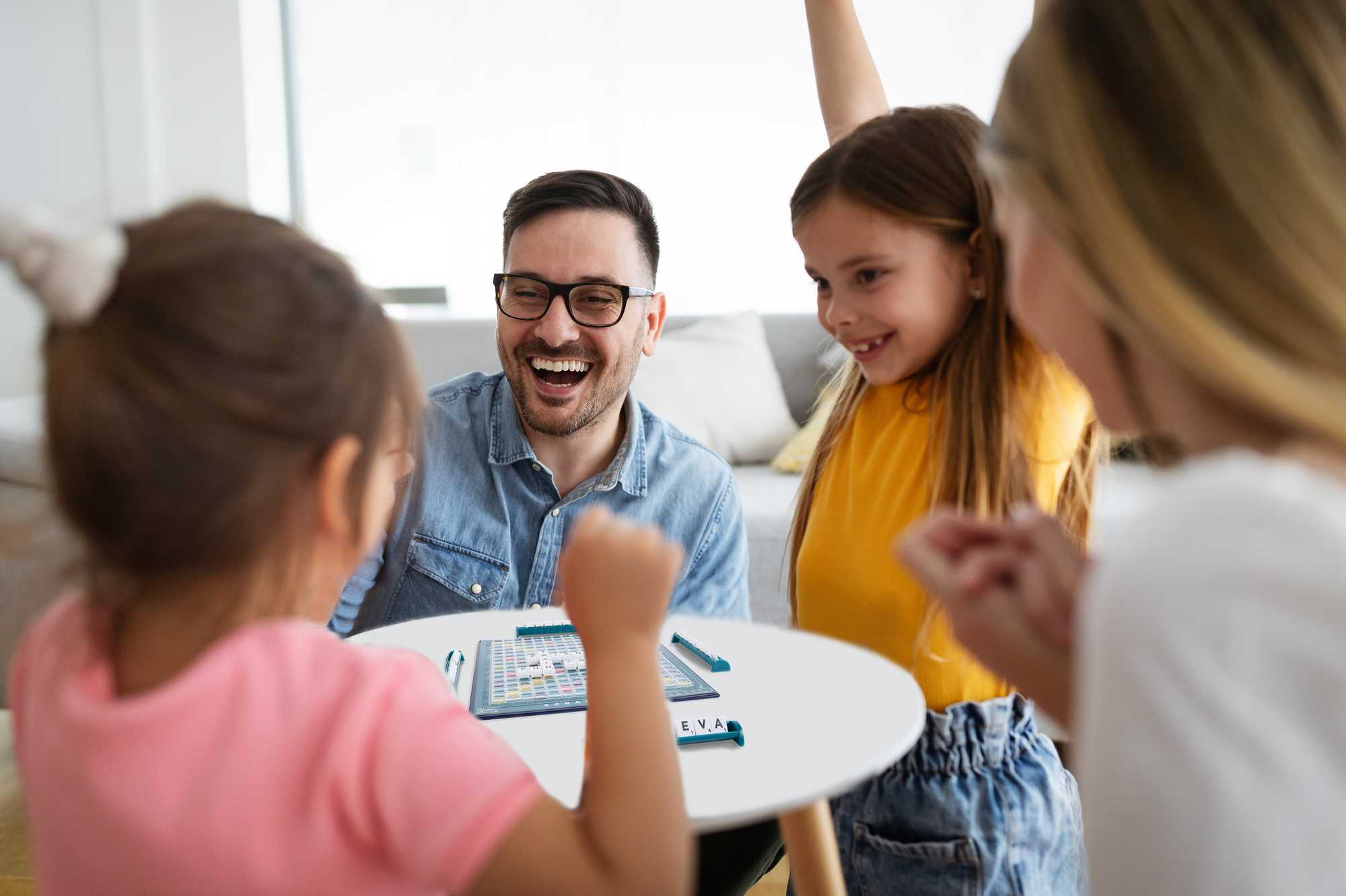 Een gezin speelt een bordspel. Een man lacht. Kinderen en een vrouw zitten rond een tafel. In het midden staat een spelbord.