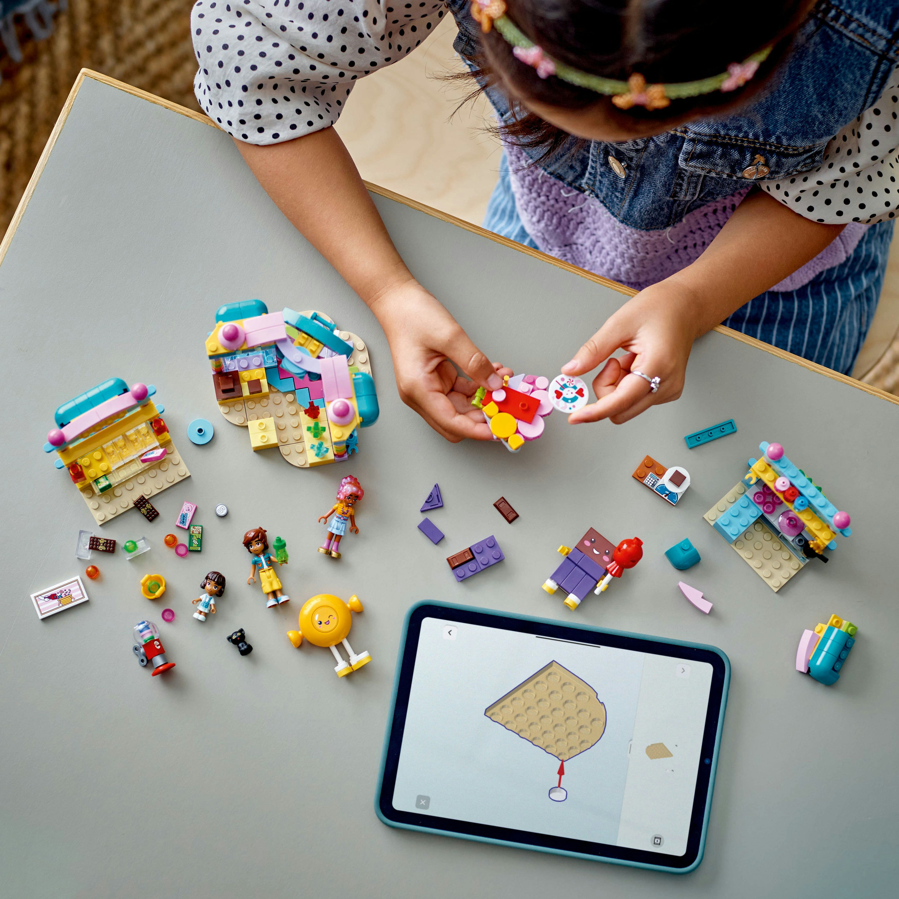 Dziecko buduje z Lego. Na stole różne zestawy Lego, figurki i iPad z instrukcjami.