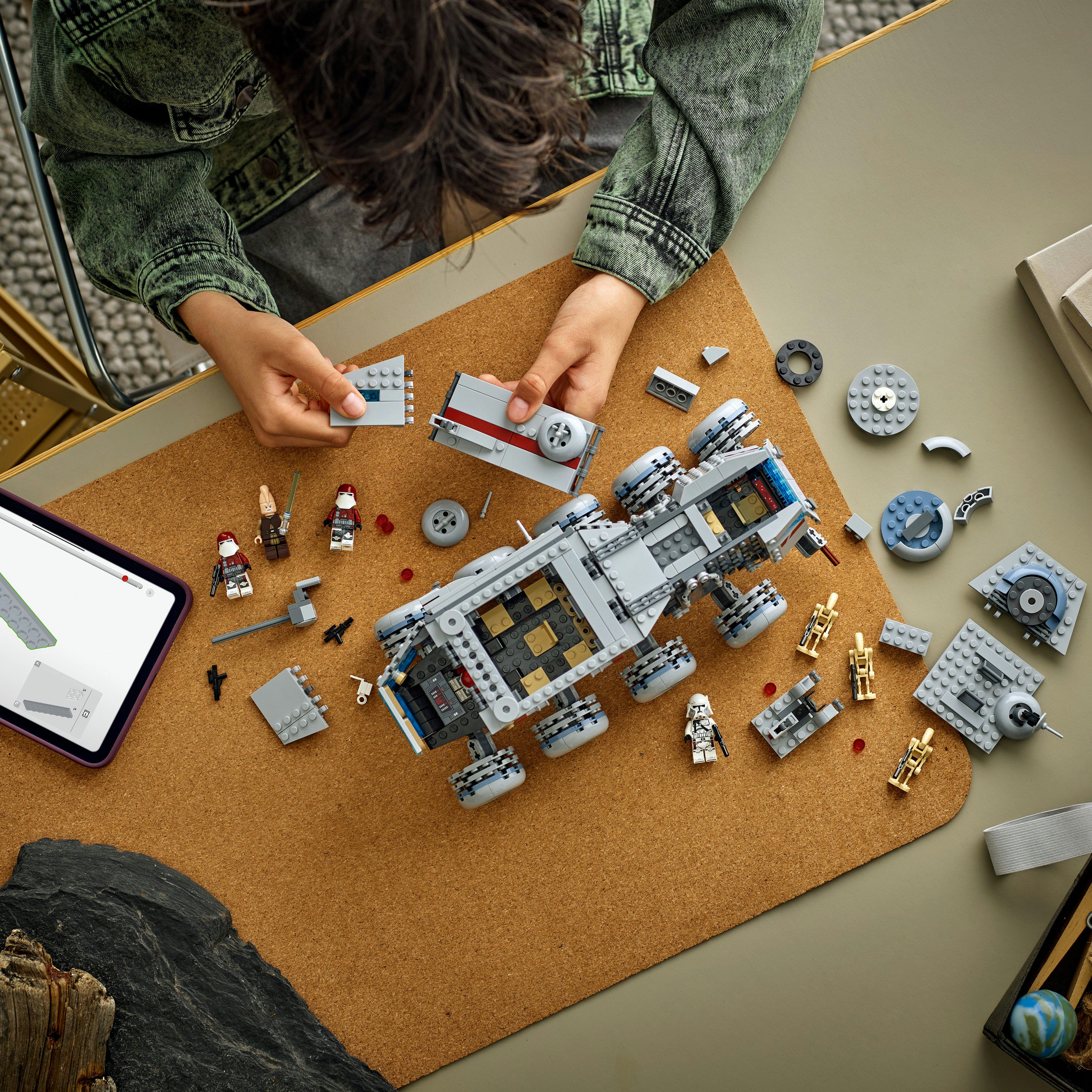 Osoba buduje zestaw Lego. Zestaw to szary pojazd z kilkoma minifigurkami i rozrzuconymi klockami Lego.