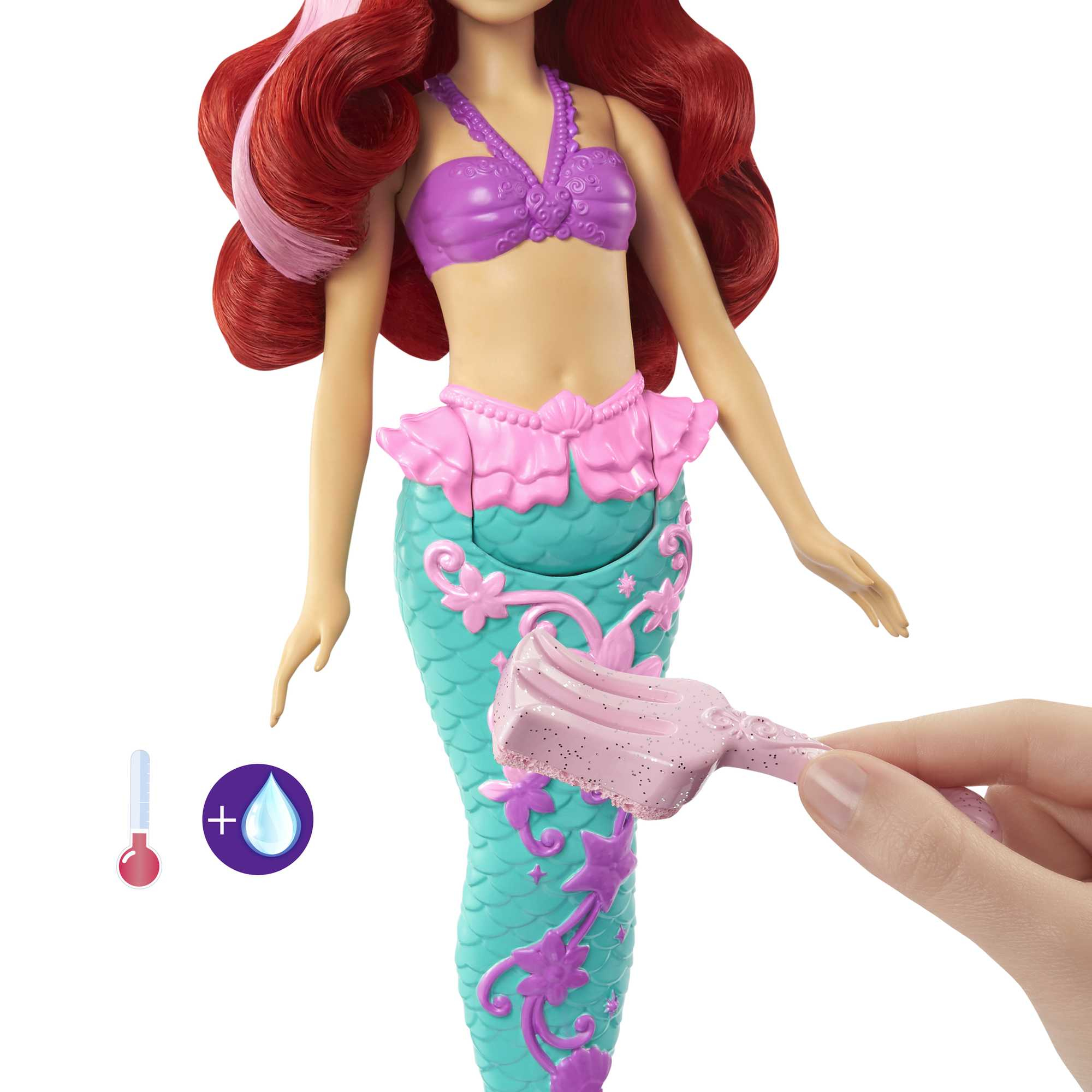Ariel-Puppe mit rotem Haar, lila Oberteil, türkisfarbenem Schwanz und rosa Zubehör. Eine Hand hält eine rosa Bürste.