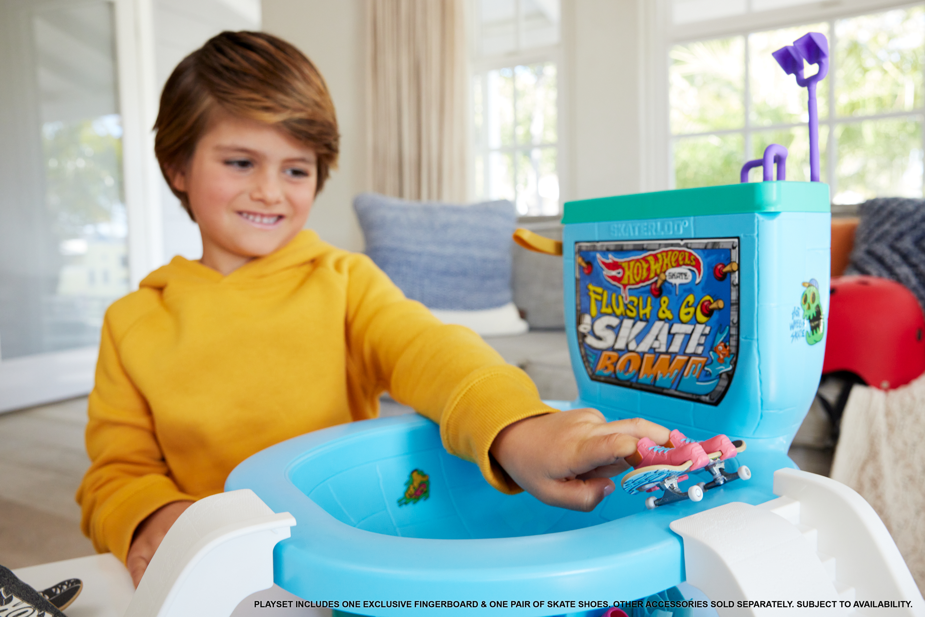 Een jongen in het geel speelt met een blauwe Hot Wheels skate bowl speelset, met een roze skateboard.