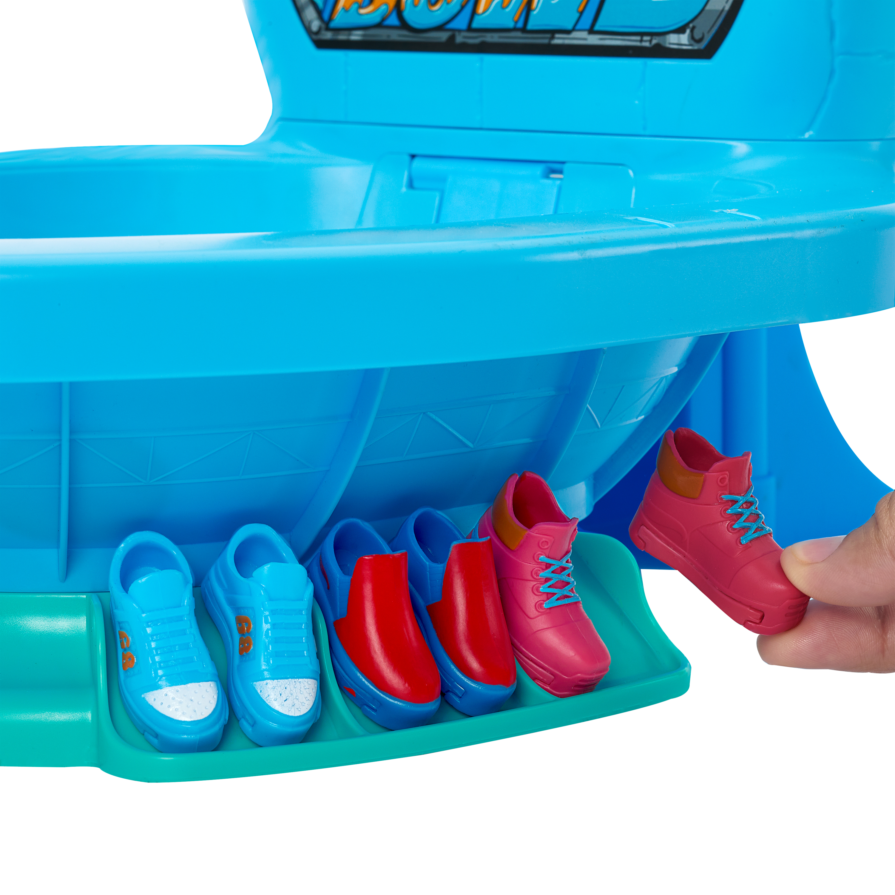 Een hand die een roze schoen vasthoudt naast andere paren kleurrijke speelgoedschoenen op een blauwe speelgoedstructuur.