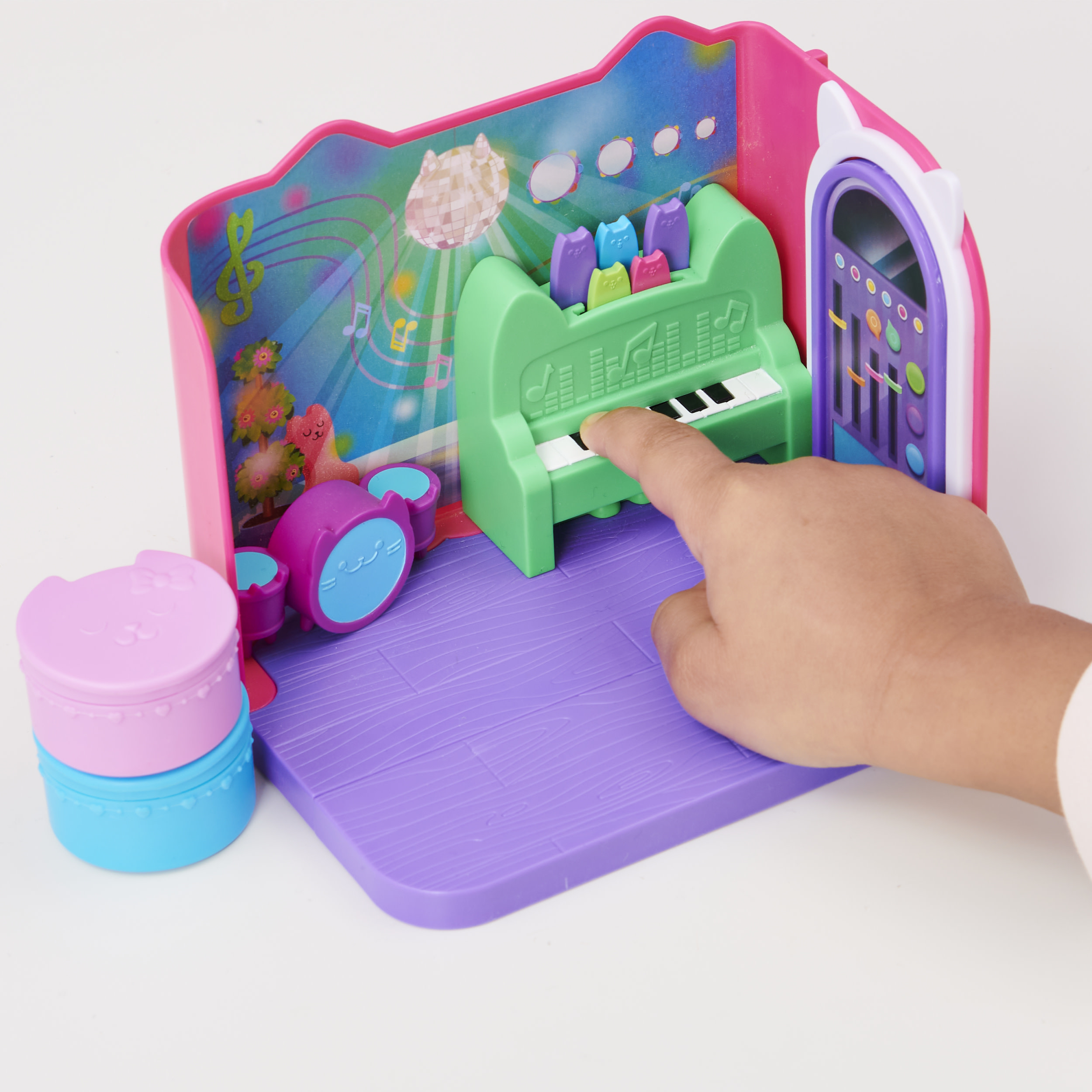 Dłoń dziecka na zielonym pianinie zabawkowym w różowym pokoju z motywem kota, z zestawem perkusyjnym i pudełkiem prezentowym.