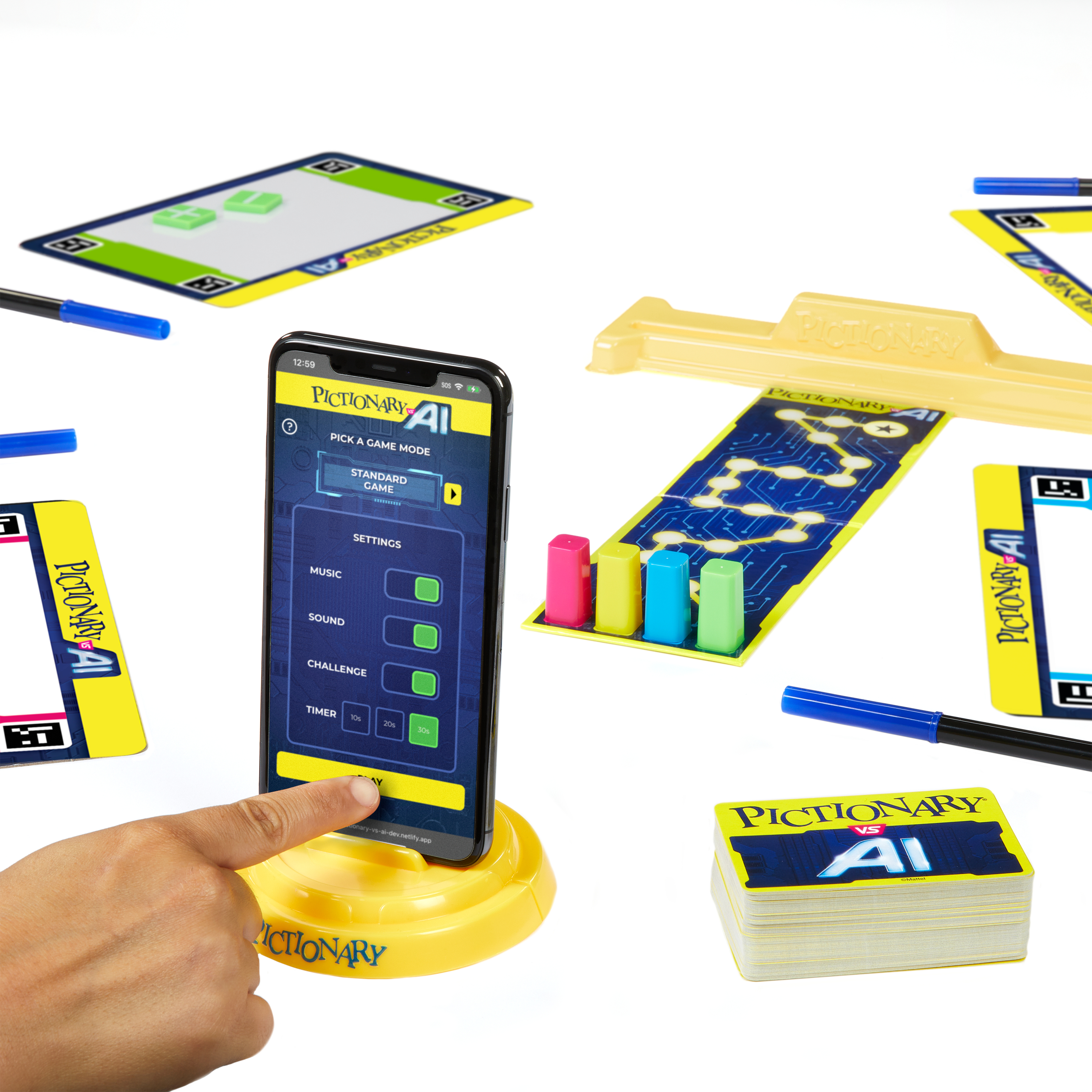 Konfiguracja gry Pictionary AI z telefonem, kartami, długopisami i elementami gry. Ręka dotyka ekranu.