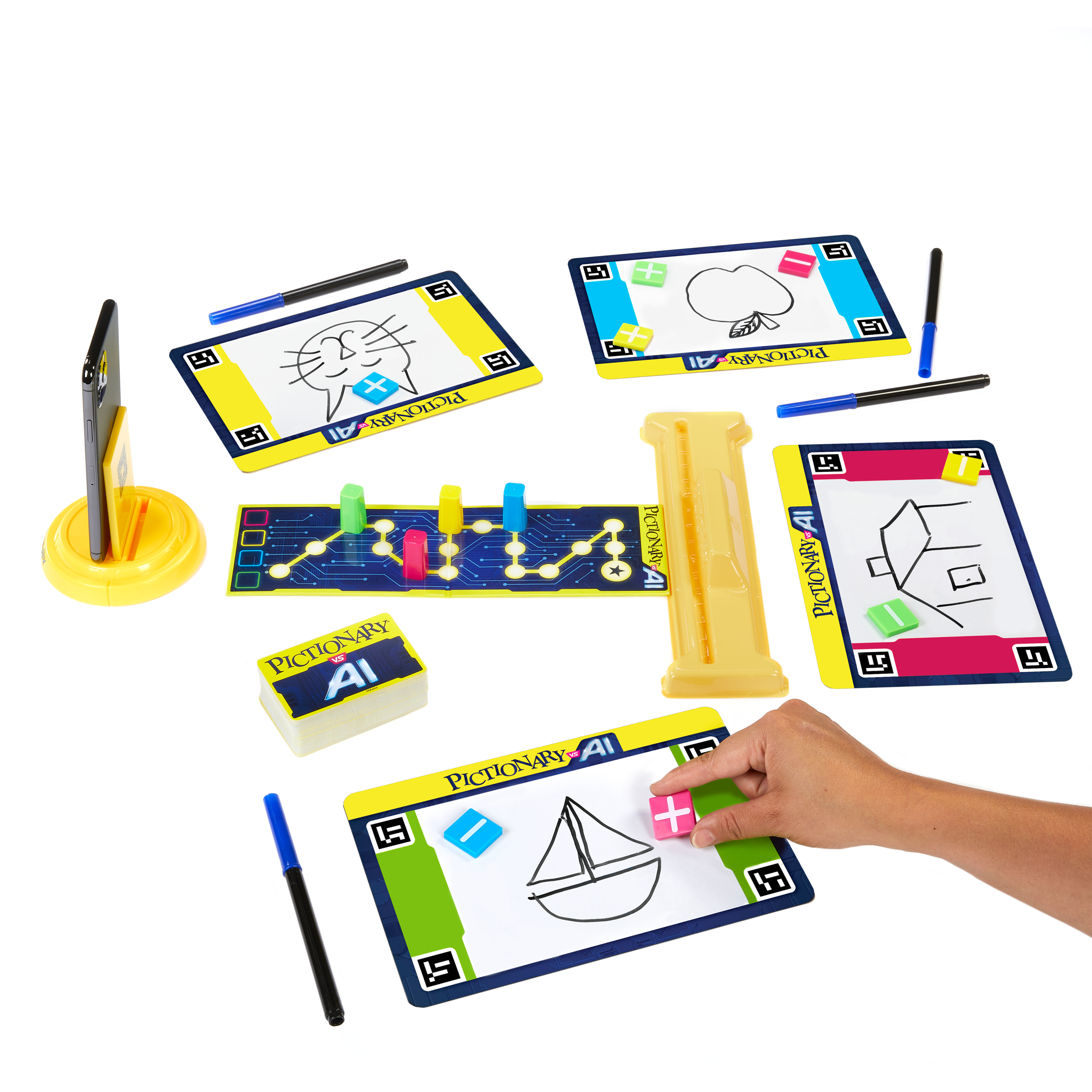 Zestaw gier Pictionary AI z rysunkami, długopisami, planszą i podstawką pod telefon. Ręka umieszcza różowy klocek.