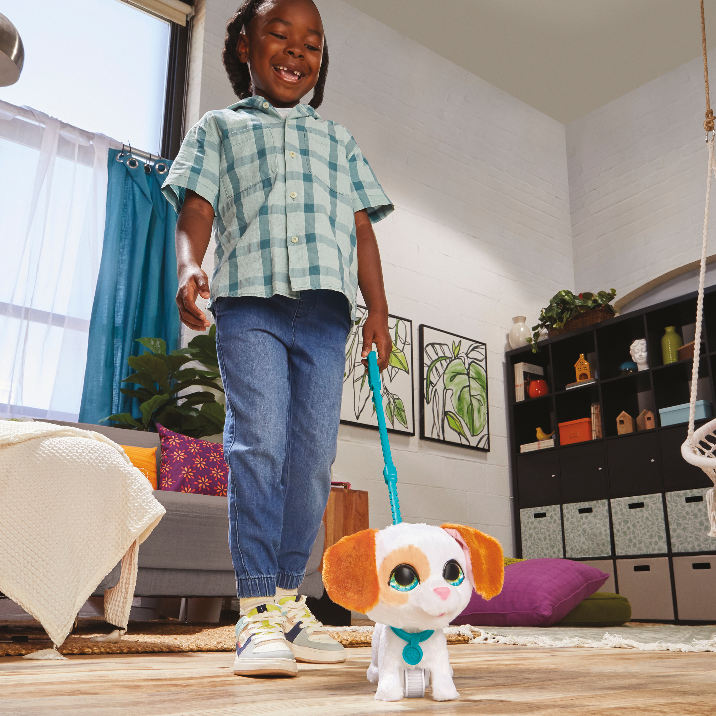 Uśmiechnięte dziecko prowadzi zabawkę szczeniaka na smyczy. Szczeniak ma białe futro, pomarańczowe uszy i niebieską obrożę.