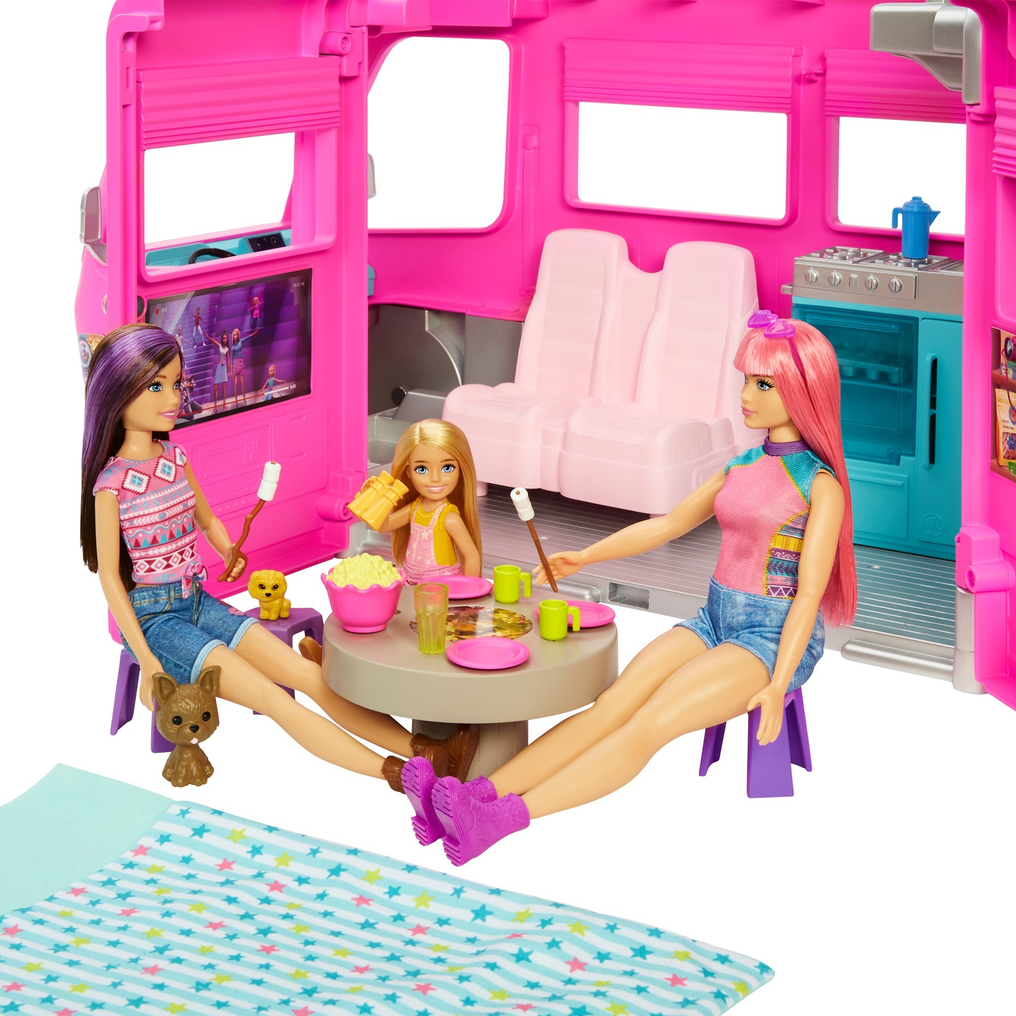Tre bambole Barbie sono in un camper rosa. Sono sedute attorno a un tavolo con degli snack, godendosi un pasto insieme.