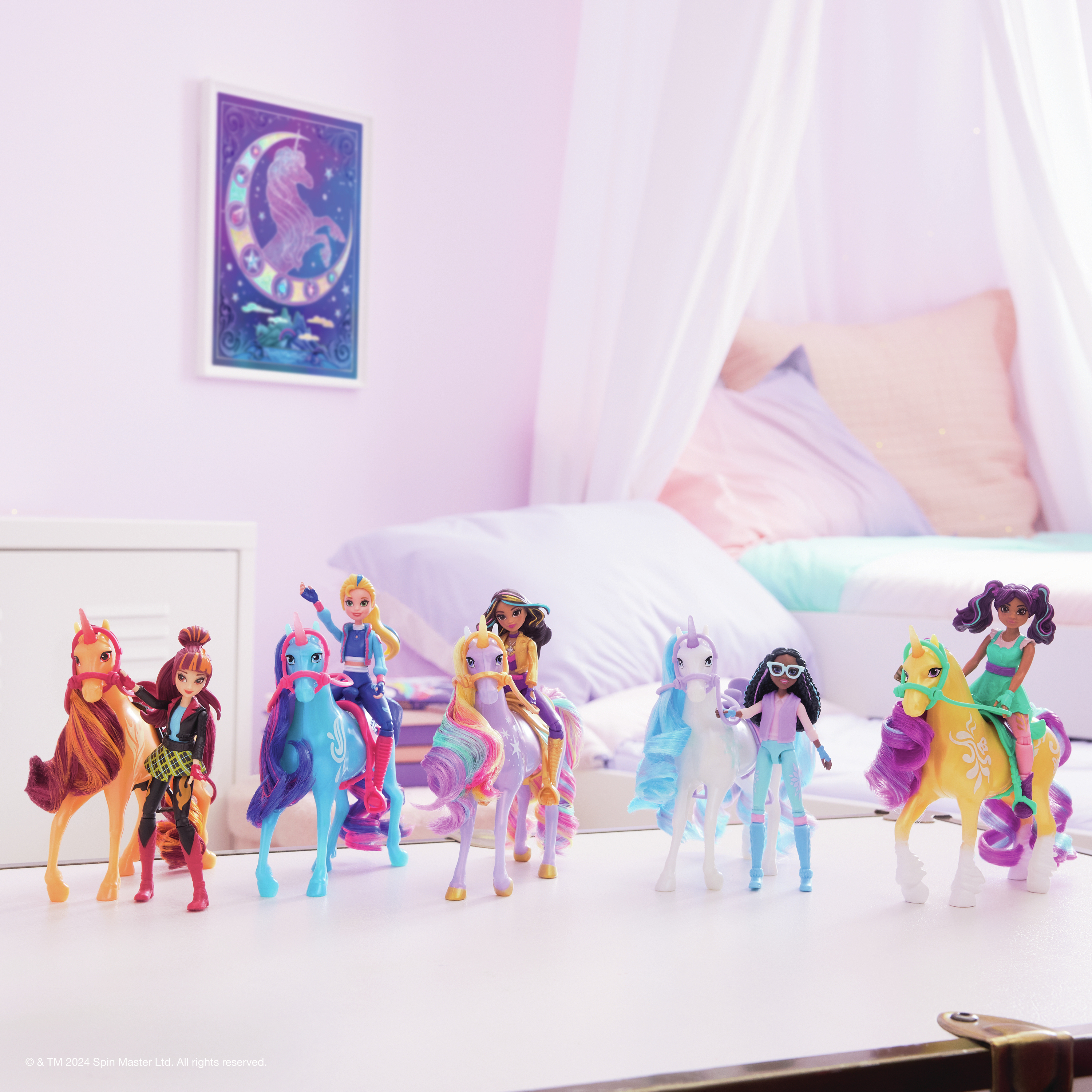 Scena z zabawkami jednorożców i lalkami. Lalki jeżdżą na jednorożcach. Tło to różowa ściana i łóżko.