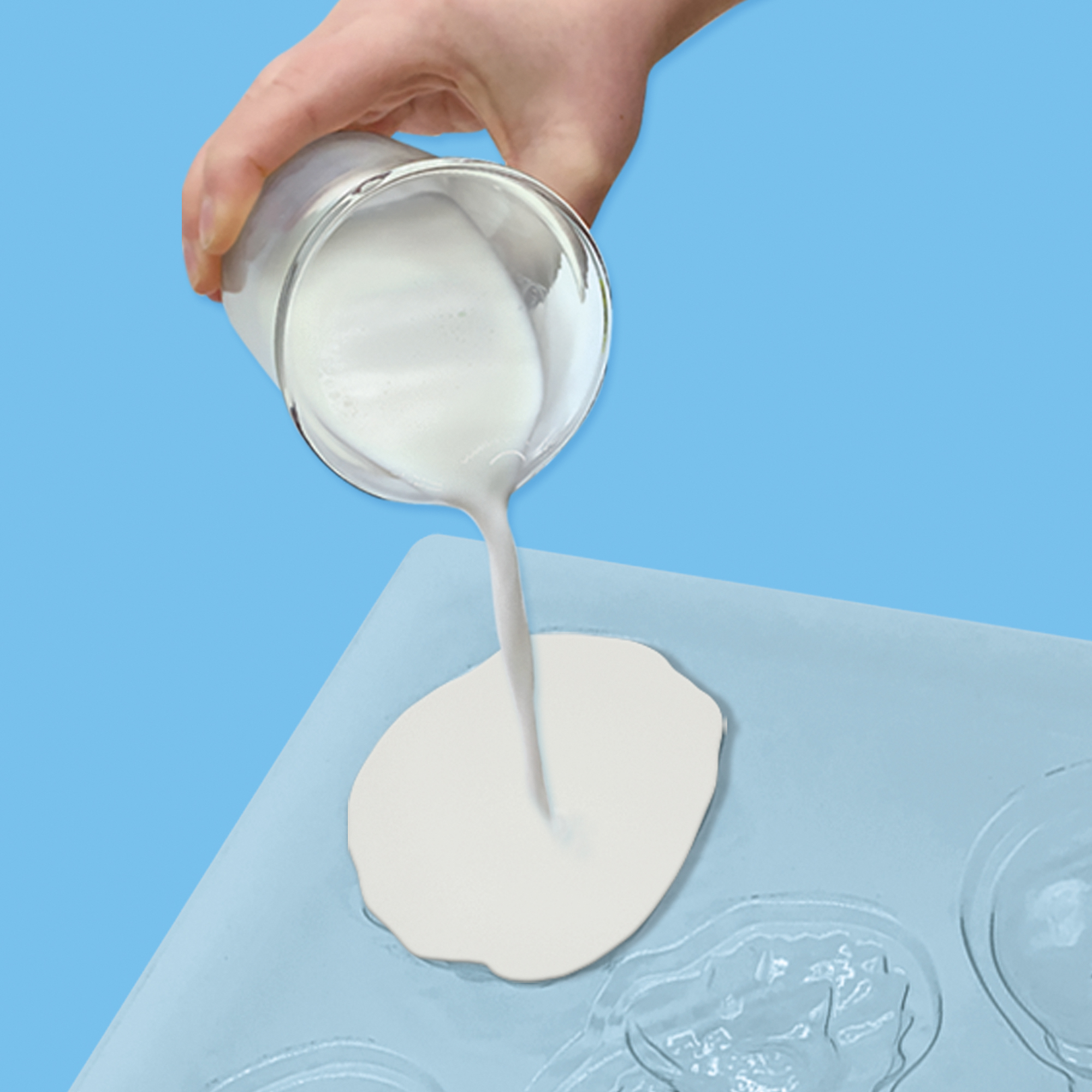 Ręka wlewa białą ciecz ze szklanki do niebieskiej formy. Tło jest jasnoniebieskie.