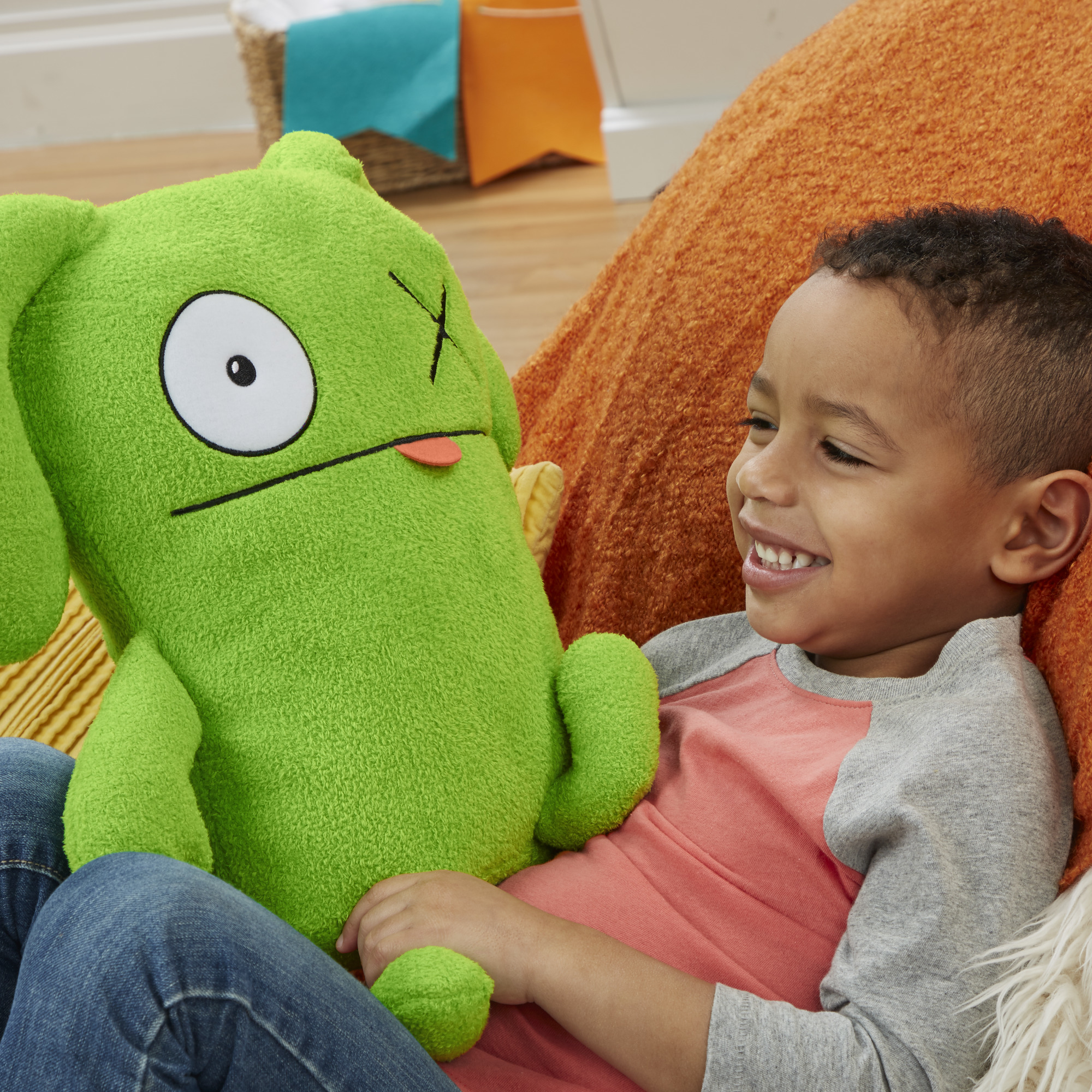 Uśmiechnięty chłopiec z zieloną pluszową zabawką. Chłopiec ma na sobie różową koszulę. Pluszak jest zielony z dużym okiem i językiem.