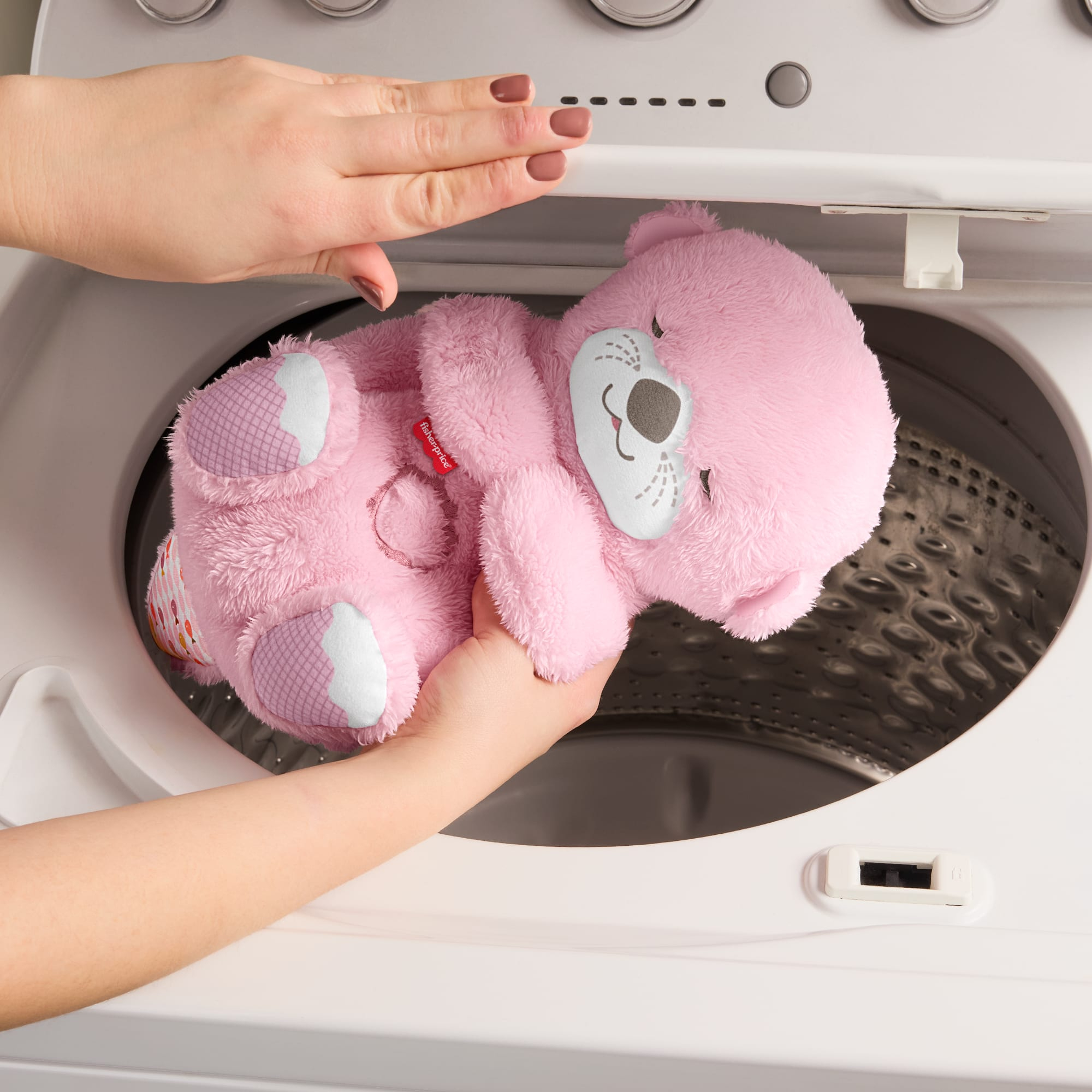 Ein rosa Teddybär wird von zwei Händen in eine Waschmaschine gelegt.