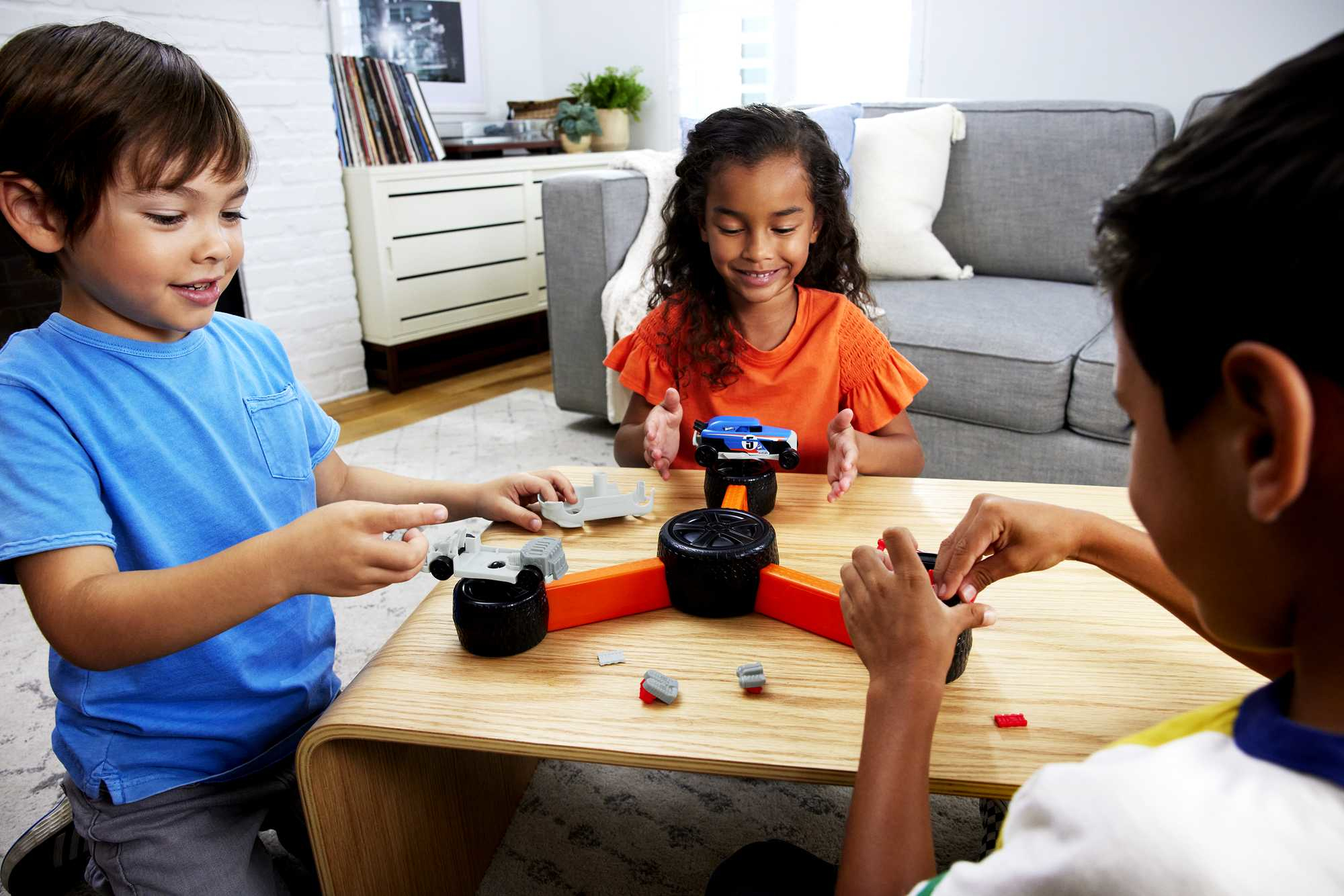 Tres niños juegan con un coche de juguete en una mesa de madera. Un coche azul está sobre un neumático negro. Los niños sonríen.