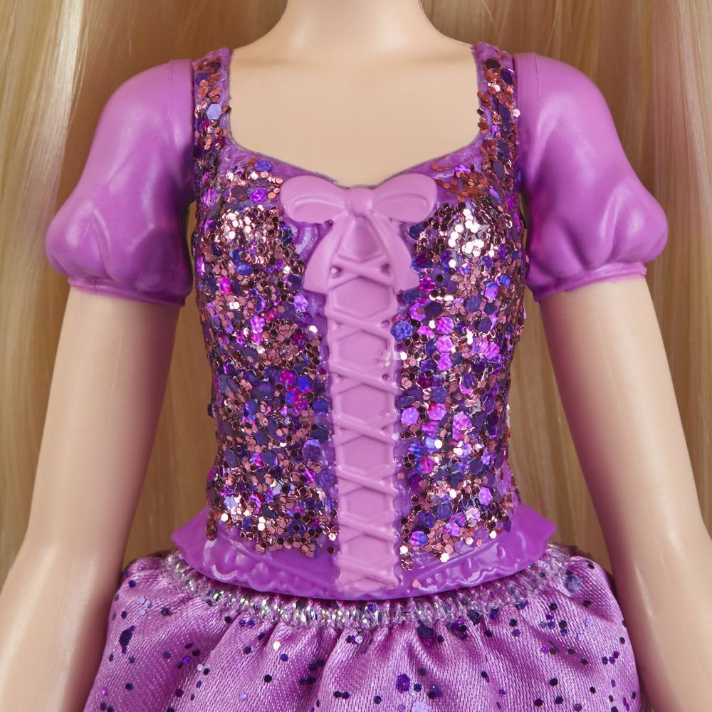 Una bambola con un vestito viola con corpetto di paillettes e fiocco. Lo sfondo sfocato mostra capelli biondi.