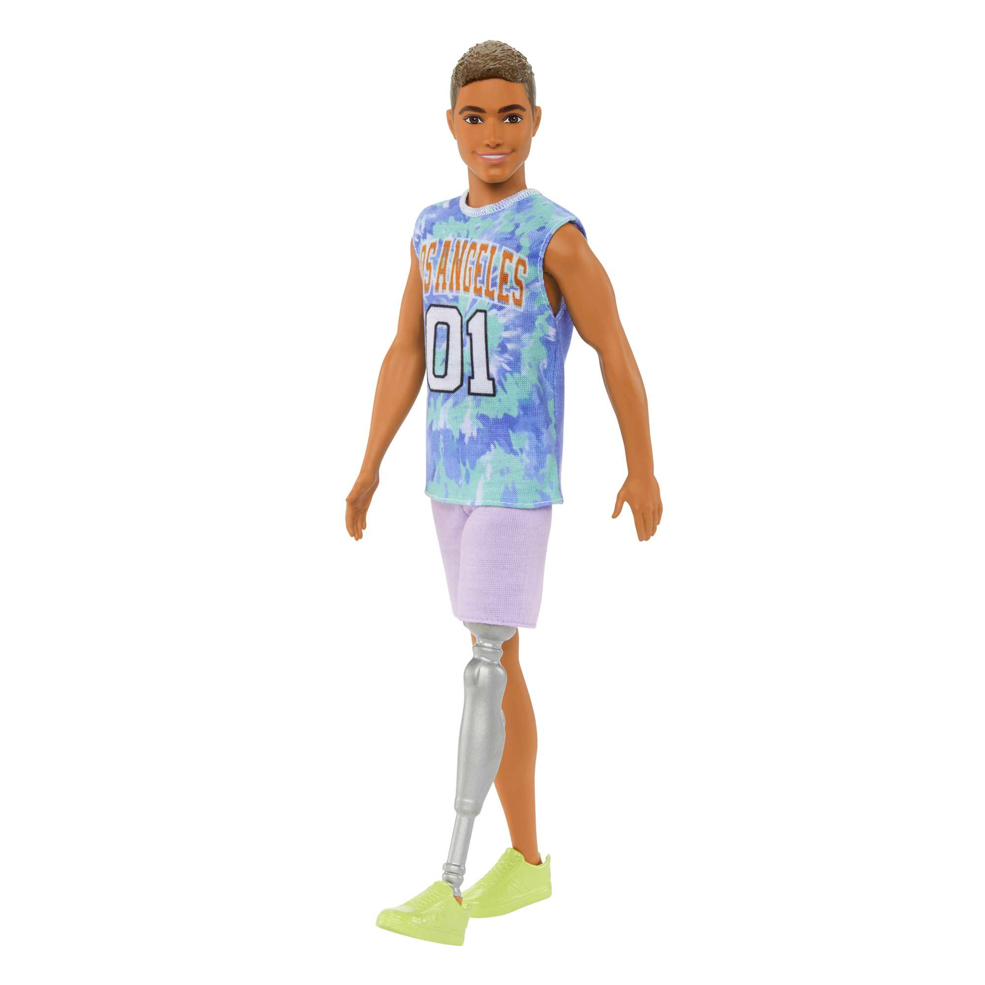 Lalka Ken z protezą nogi ma na sobie niebieski top w stylu tie-dye, fioletowe szorty i limonkowo-zielone buty, uśmiechając się na białym tle.
