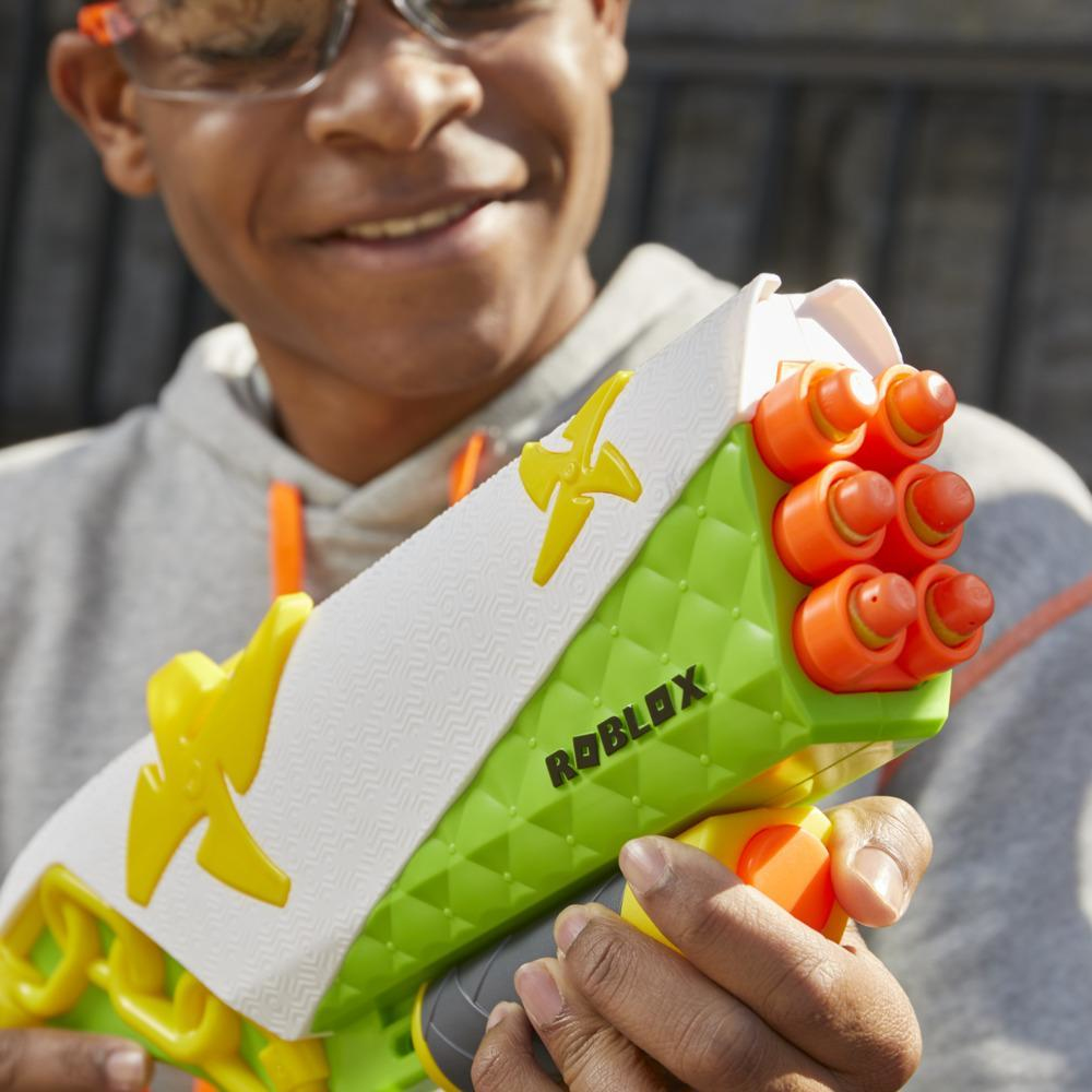 Osoba trzyma zielony, biały i pomarańczowy pistolet-zabawkę Roblox. Osoba się uśmiecha. Tło jest rozmyte.
