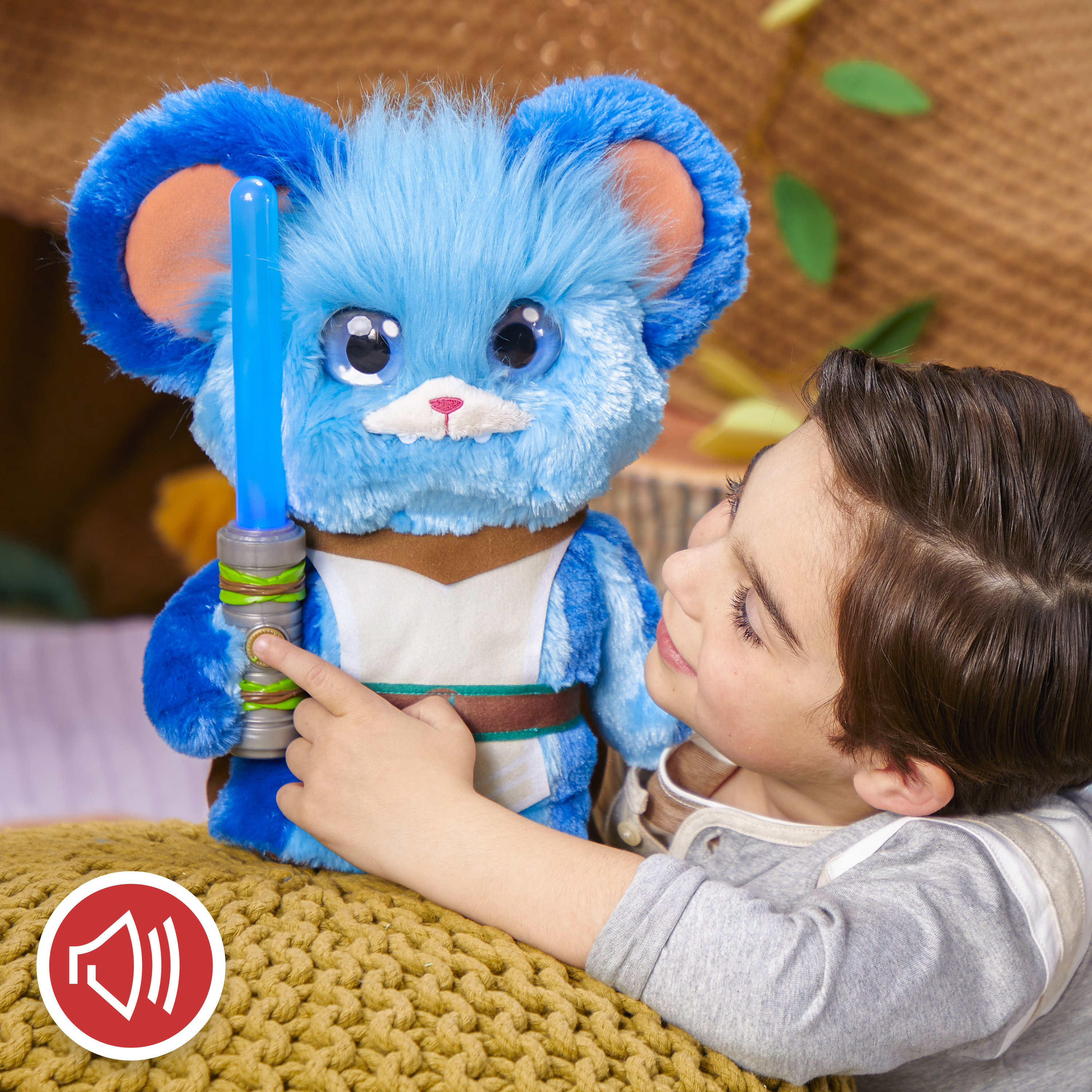 Chłopiec dotyka niebieskiej zabawki myszy trzymającej miecz świetlny. Mysz ma duże oczy. Żółta poduszka jest na pierwszym planie.