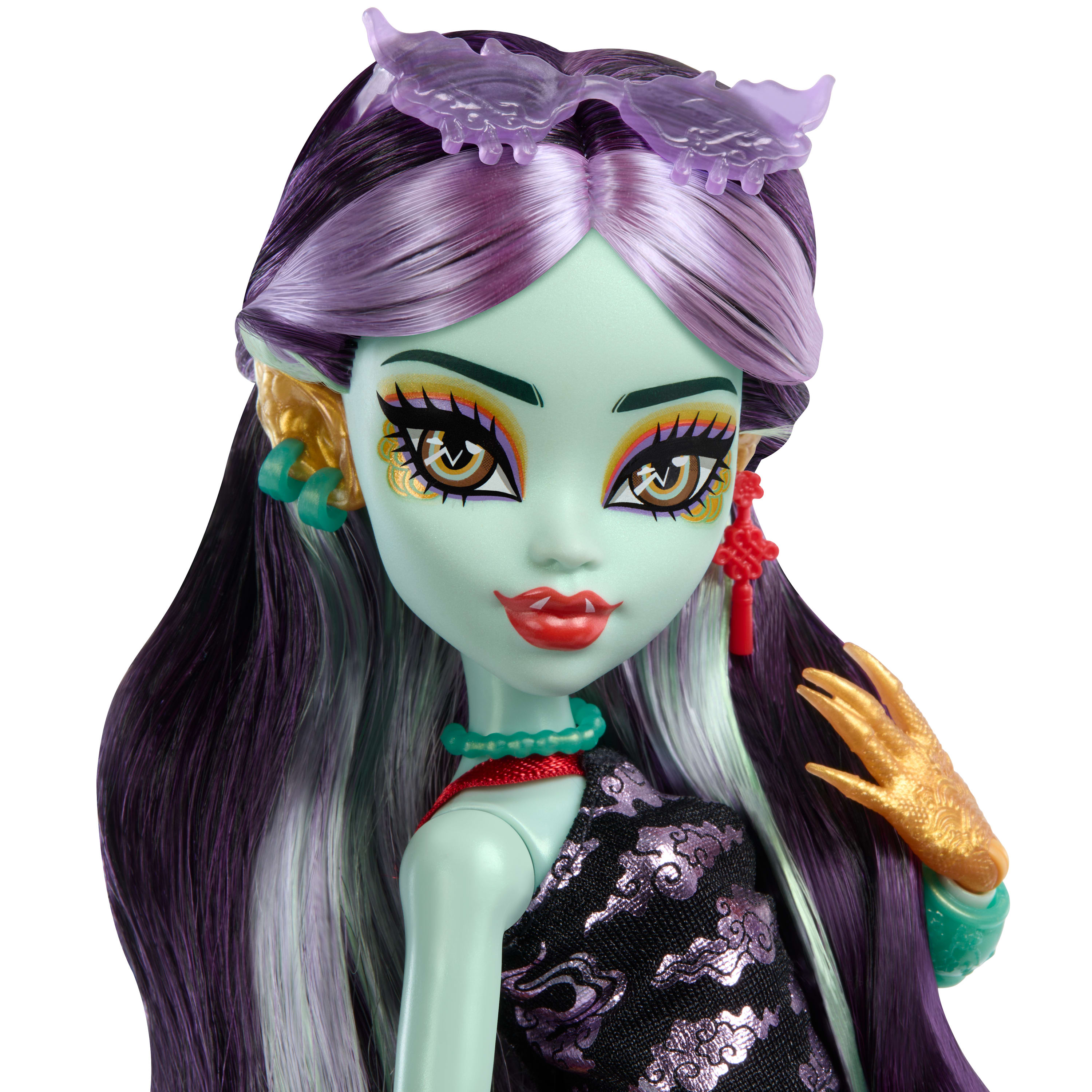 Muñeca con piel verde, cabello morado y maquillaje elaborado. Viste un vestido negro y accesorios dorados.