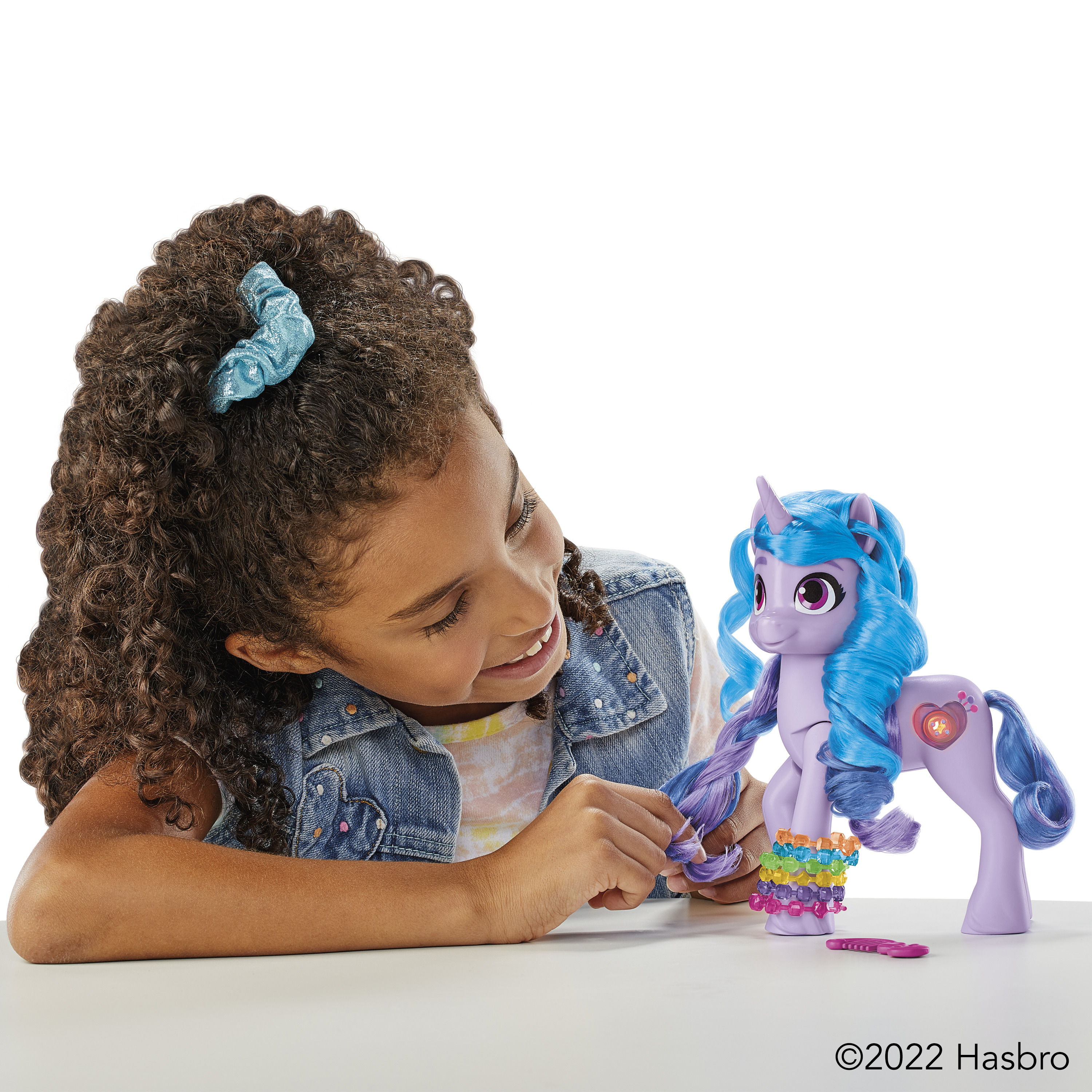 Una niña mira un poni de juguete. El poni es morado, tiene pelo azul y una pulsera colorida.