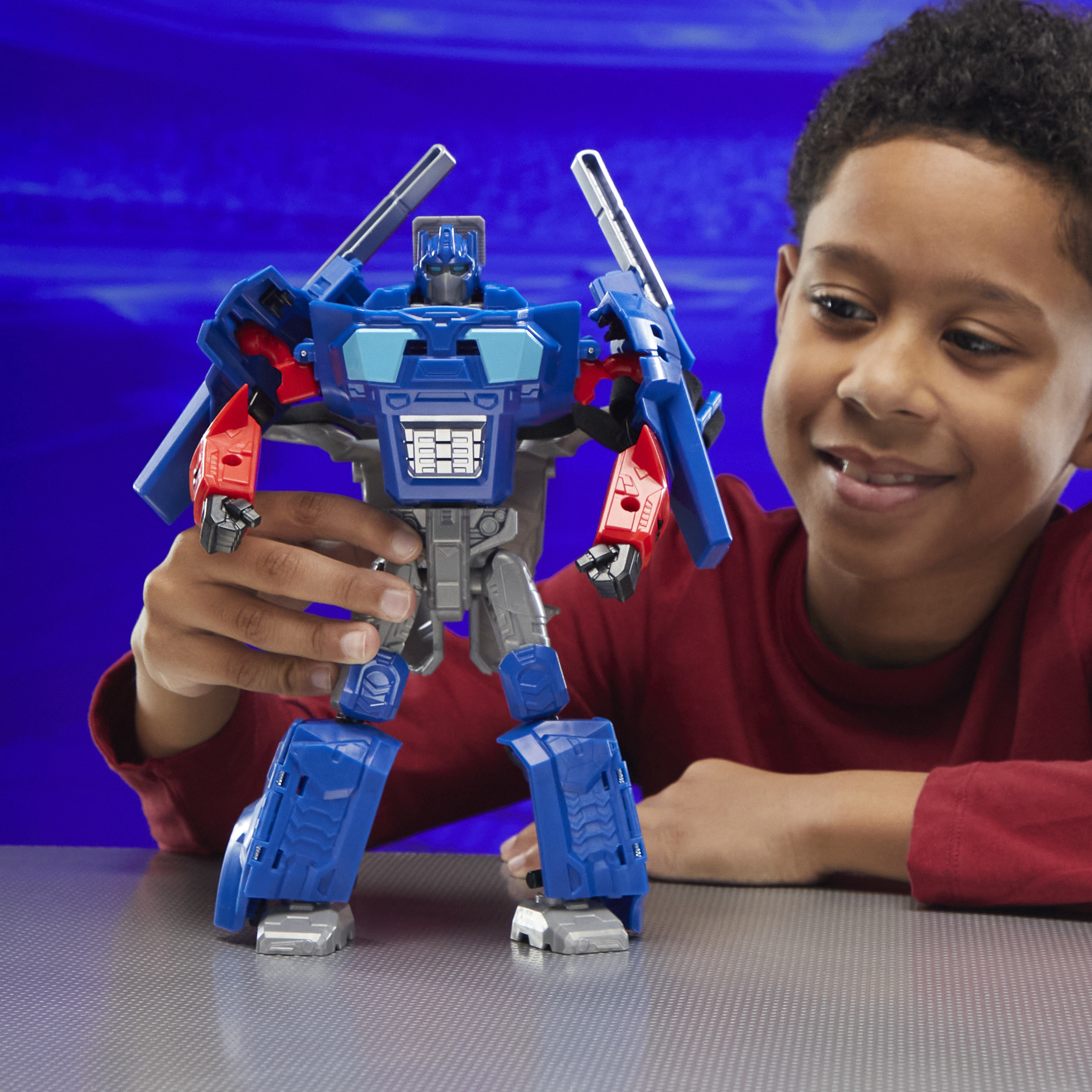 Un niño sostiene un juguete transformador azul y rojo. El fondo es un degradado azul.