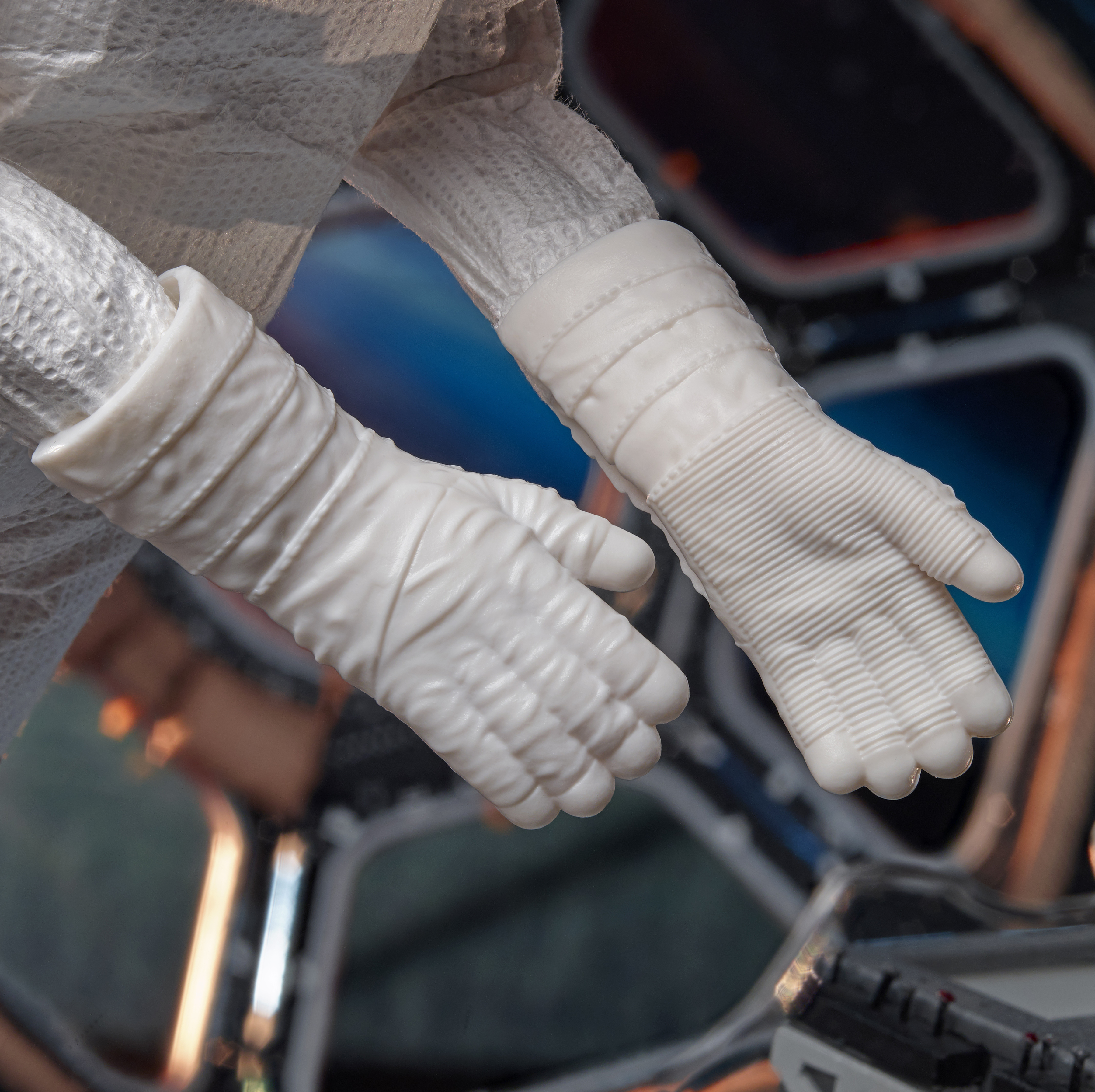 Primer plano de manos enguantadas blancas, parte de un traje espacial. El fondo muestra el interior borroso de una nave espacial.